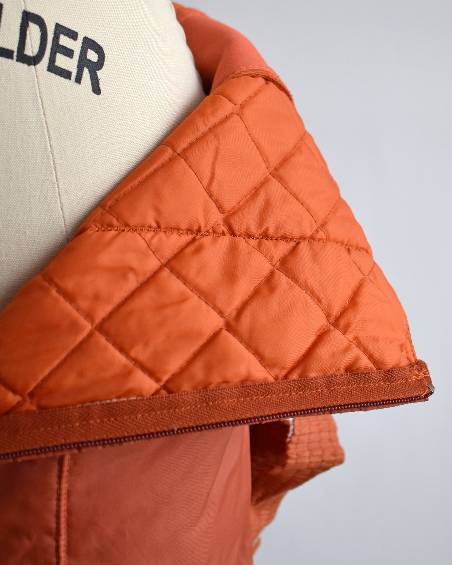 Close-up of a quilted lining on the pants of a vintage 1970s orange winter ski suit on a mannequin against a white background