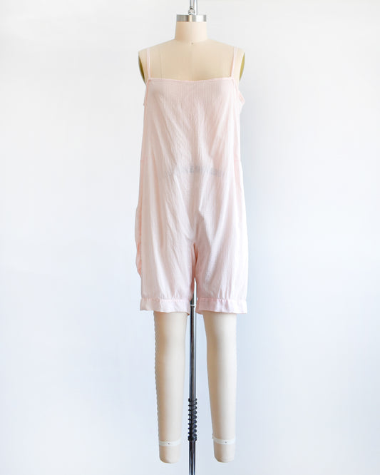 A vintage 1920s light pink chemise step in. which has spaghetti straps, square neckline, and snap buttons on the right side. The garment is on a dress form.