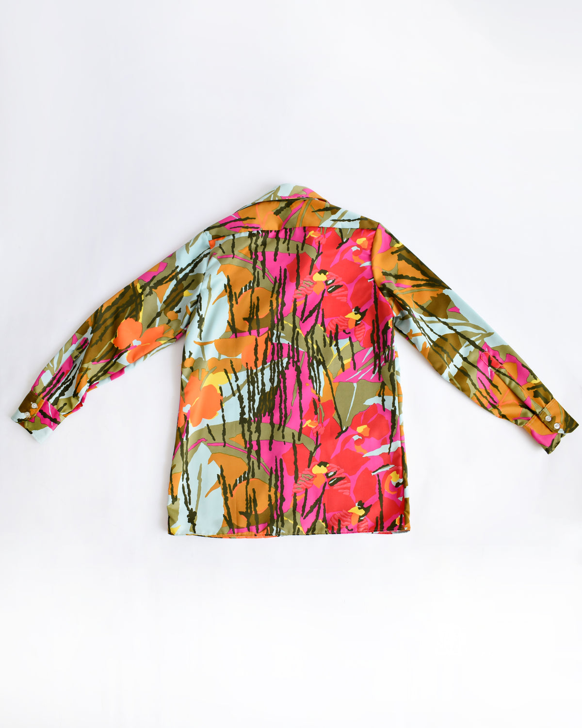 back view of a long-sleeve vintage 1970s button-up shirt with a vibrant, multicolor tropical floral print, laid flat against a plain white background.