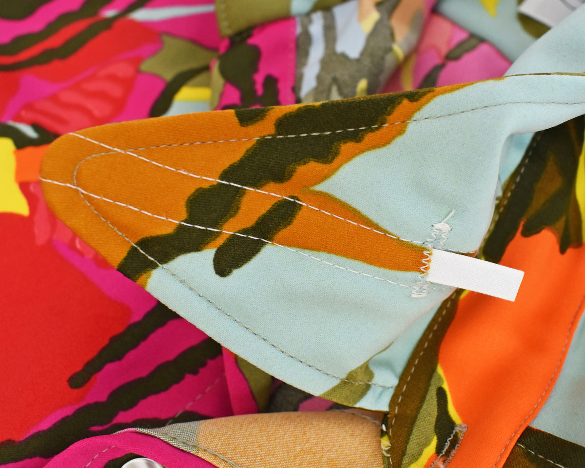 close up of the collar stays on the collar of a long-sleeve vintage 1970s button-up shirt with a vibrant, multicolor tropical floral print, laid flat against a plain white background.