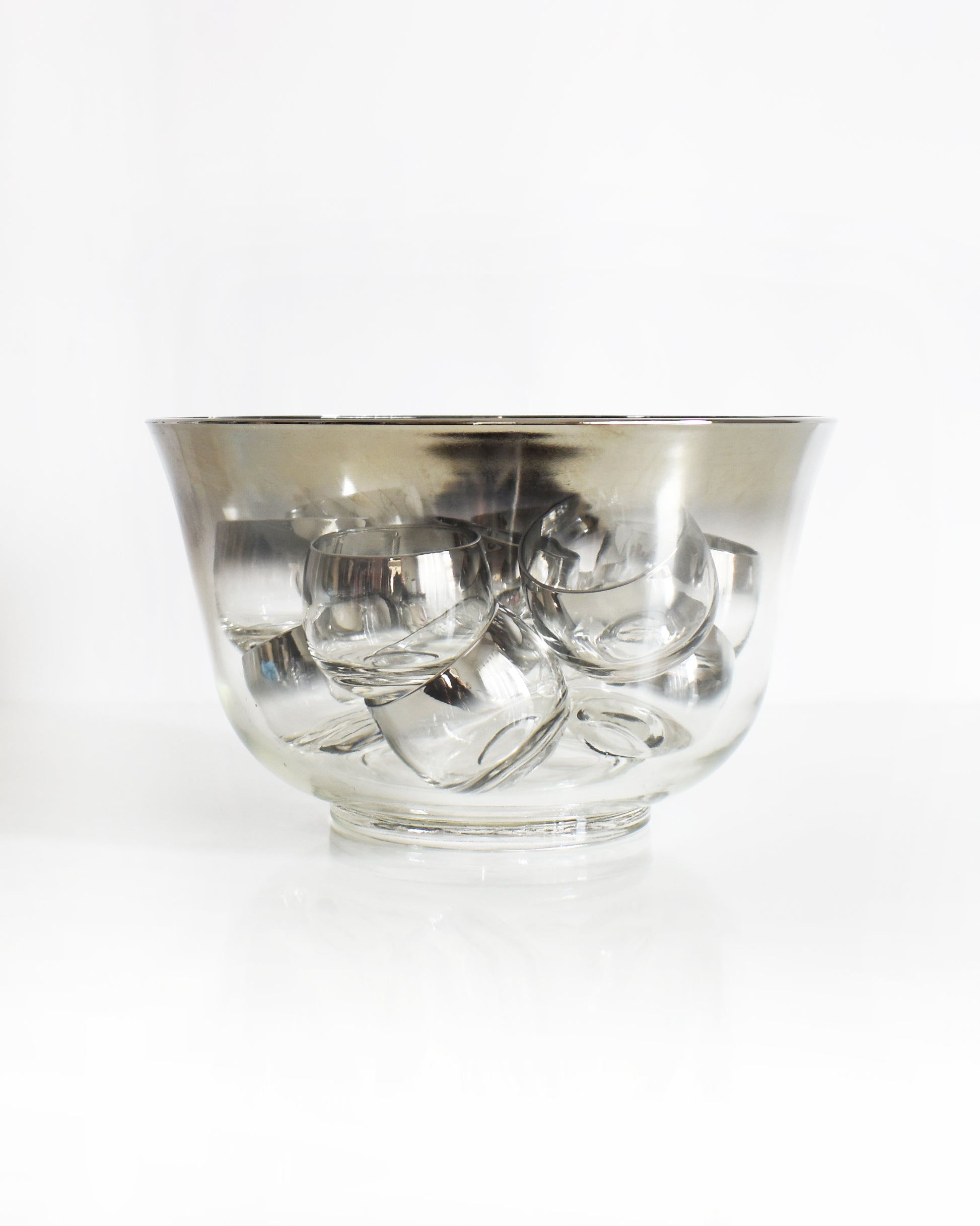 a vintage 1960s silver punch bowl and glasses set on a white background. The glasses are sitting in the punch bowl.