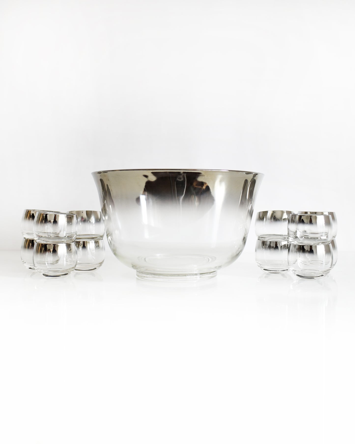 a vintage 1960s silver punch bowl and glasses set on a white background
