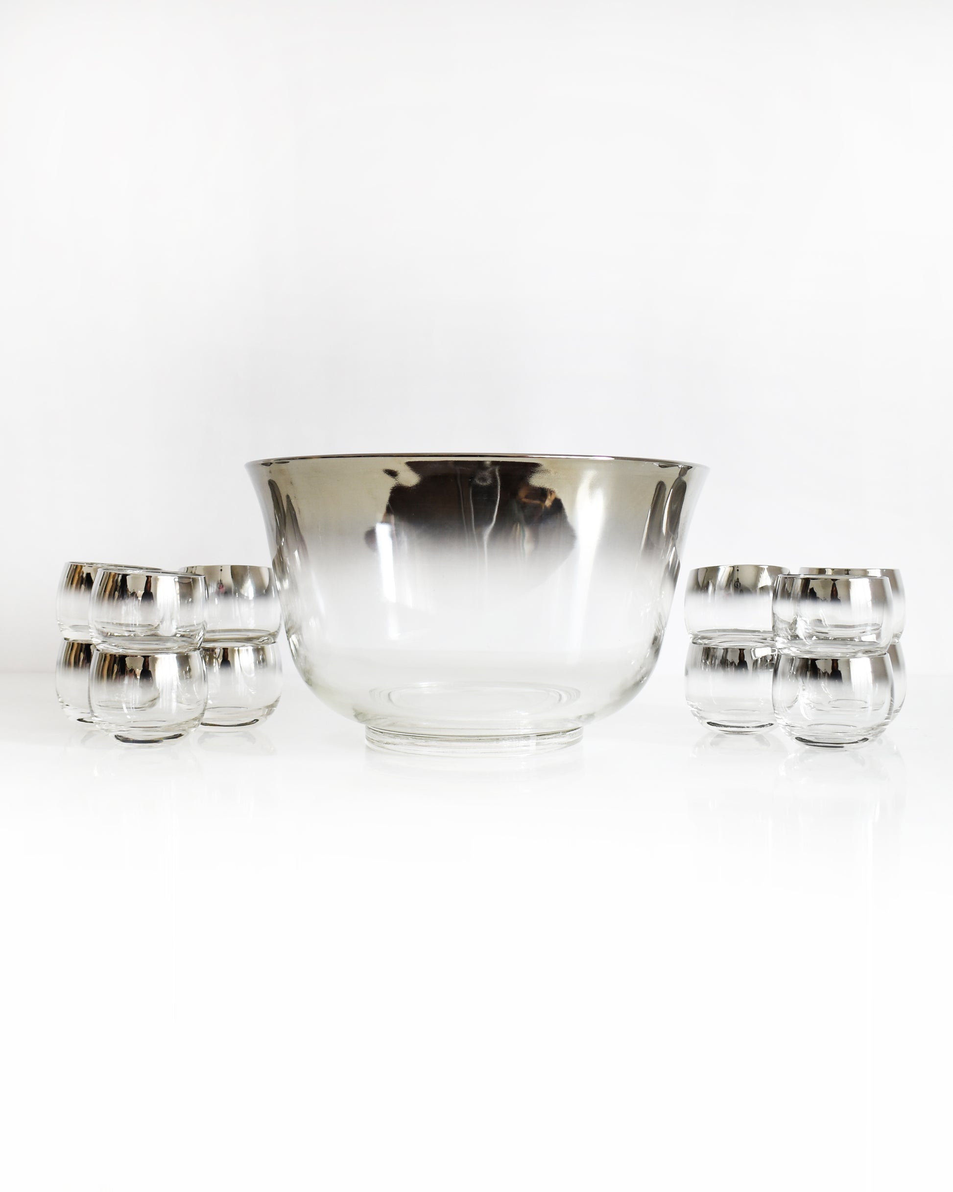a vintage 1960s silver punch bowl and glasses set on a white background