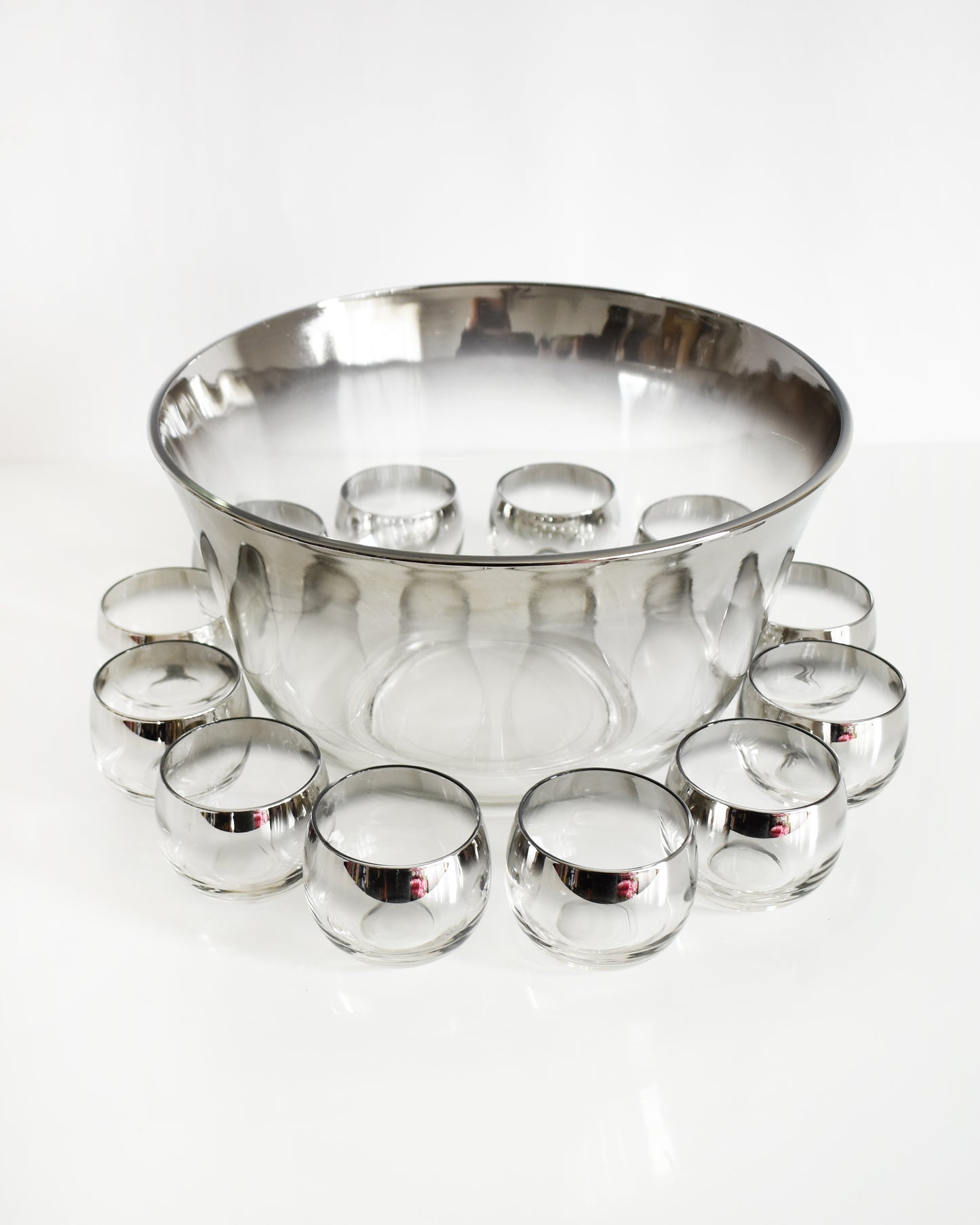 a vintage 1960s silver punch bowl and glasses set on a white background
