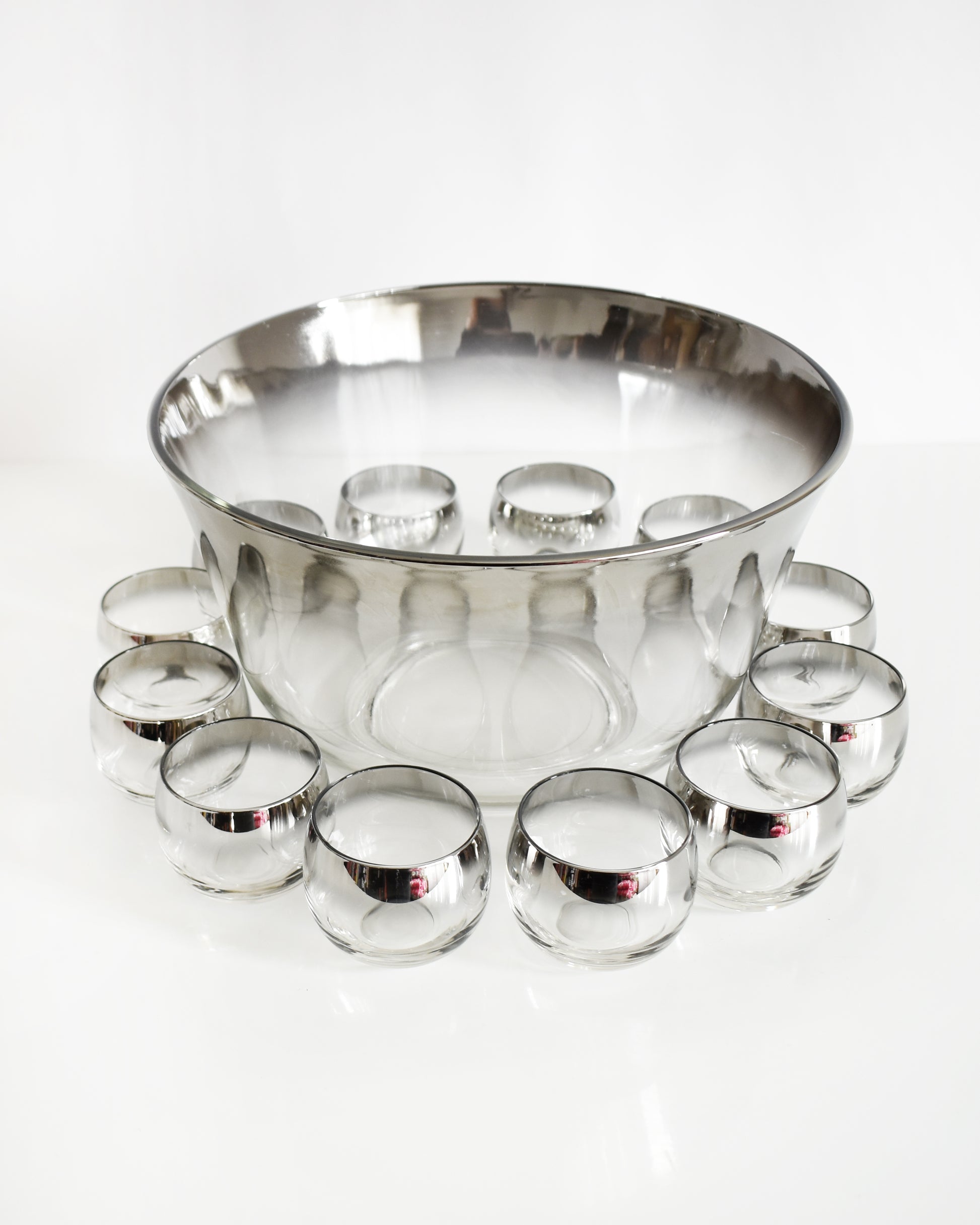 a vintage 1960s silver punch bowl and glasses set on a white background