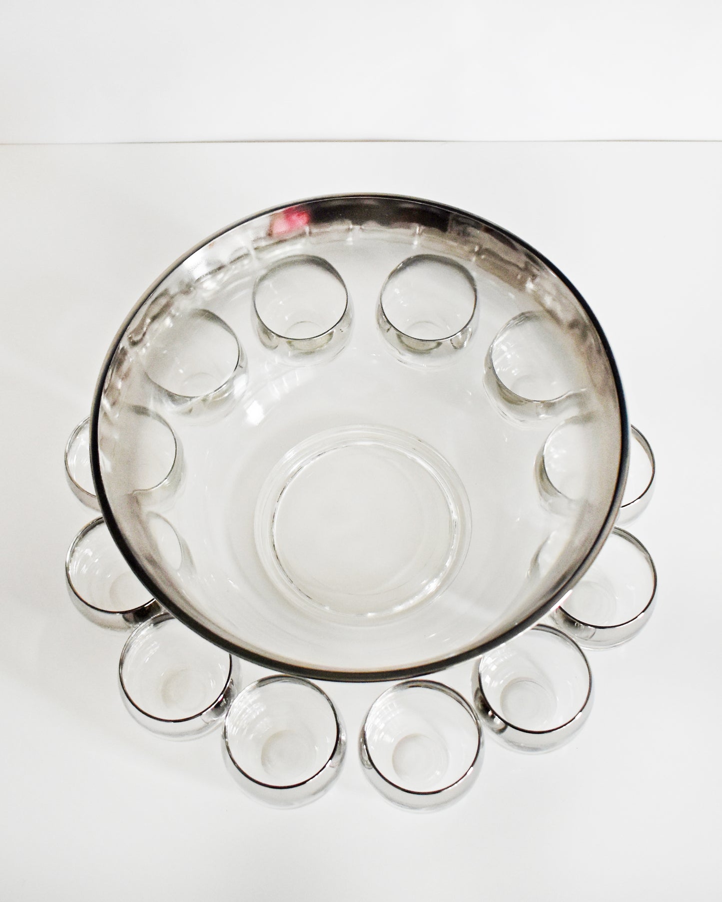overhead shot of a vintage 1960s silver punch bowl and glasses set on a white background