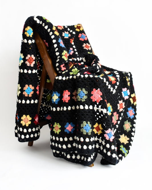 a vintage black and white crochet blanket with a colorful granny square pattern set on a chair