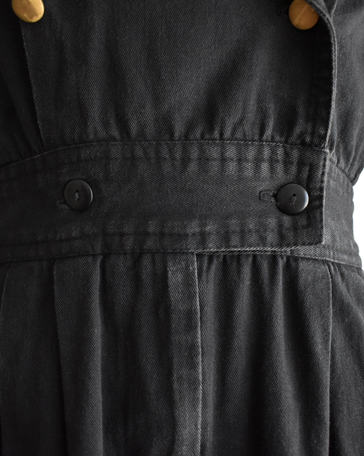 close up of the waist on a vintage 1980s black short-sleeve romper with gold-tone hardware and studded and rhinestone detailing on the collar and chest, displayed on a cream dress form against a white background.