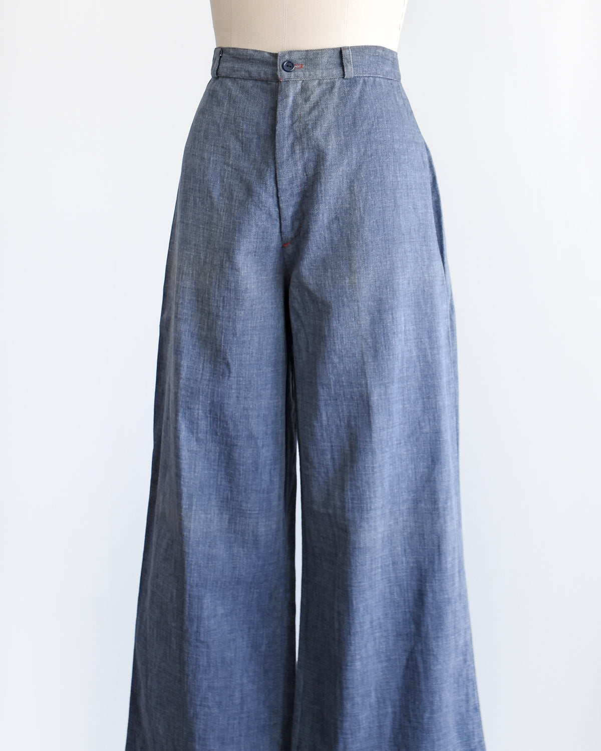 side view of A pair of wide-leg vintage 1970s denim pants displayed on a cream dress form mannequin against a plain white background.