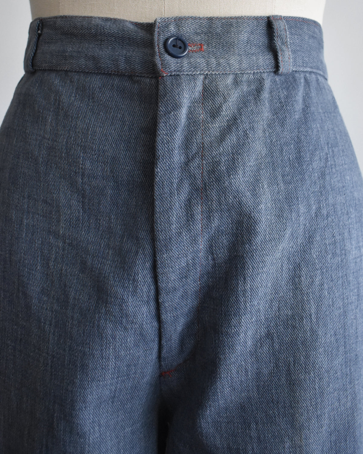 close up of the waist of a pair of wide-leg vintage 1970s denim pants displayed on a cream dress form mannequin against a plain white background.