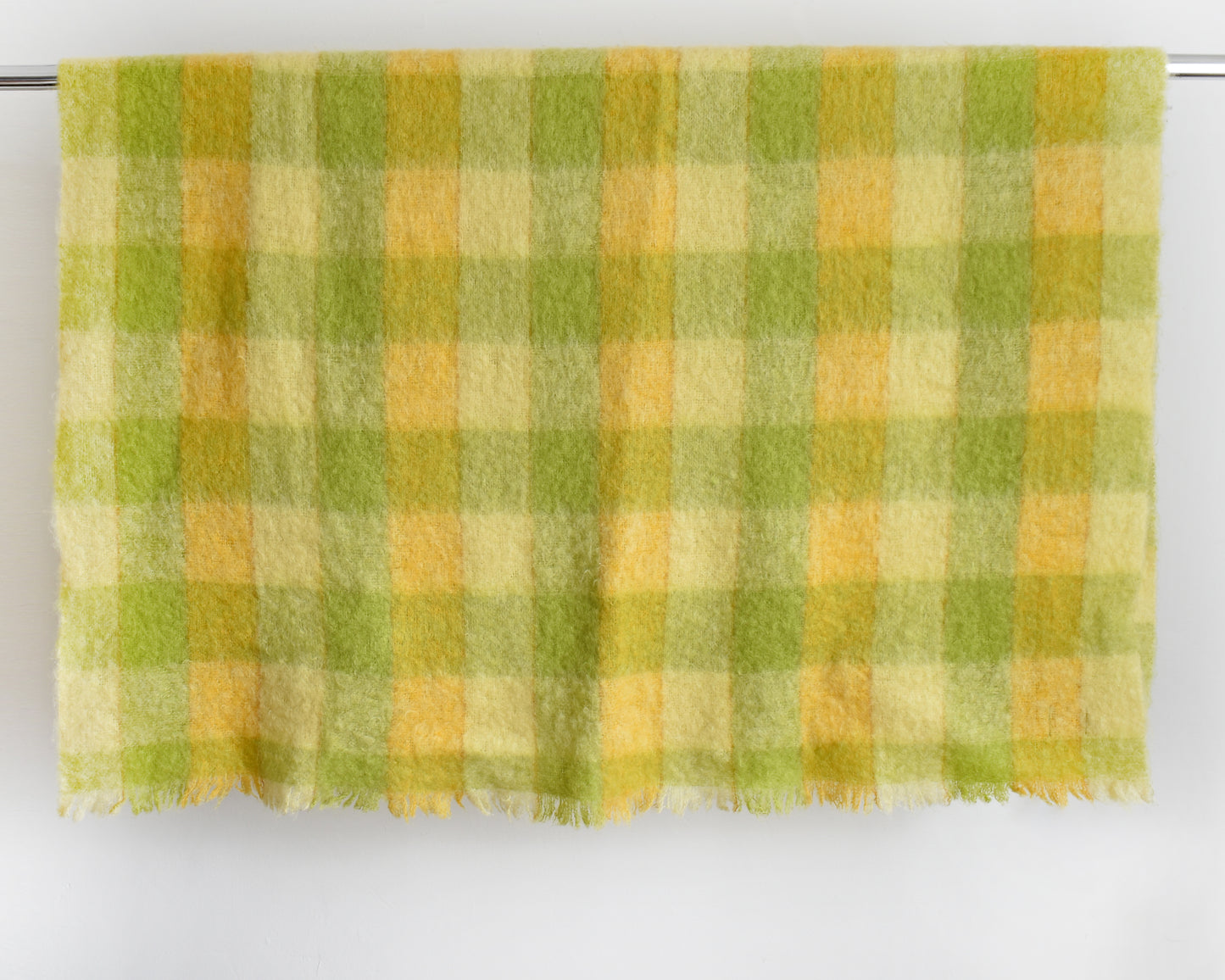 a vintage yellow and green plaid mohair wool blanket draped over a silver rod