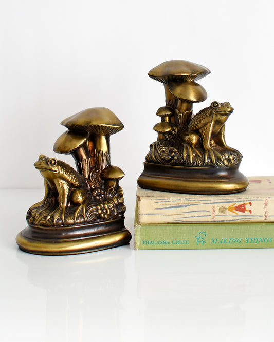 A pair of vintage brass frog and mushroom bookends. One of the bookends is on top two books