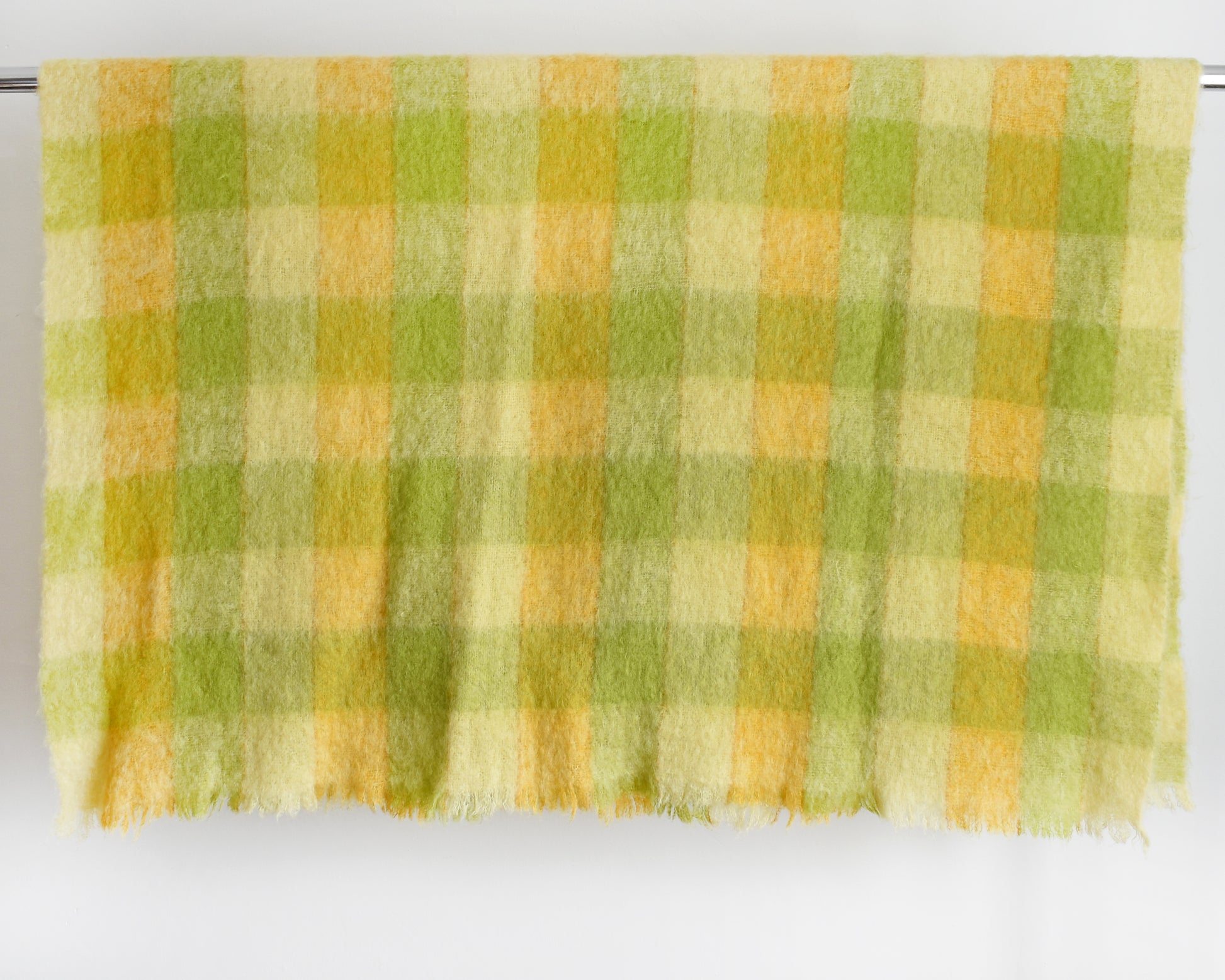 a vintage yellow and green plaid mohair wool blanket draped over a silver rod