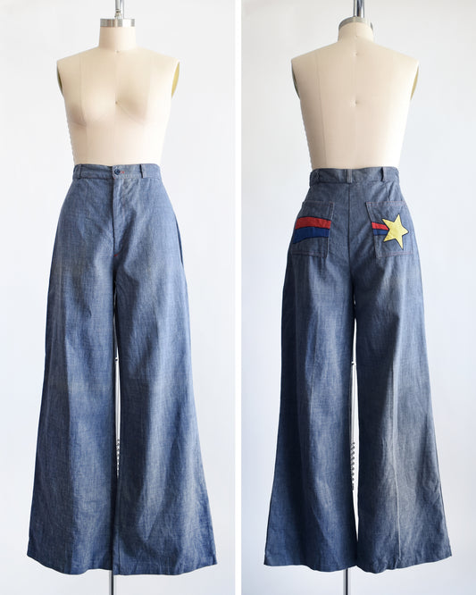 A pair of wide-leg blue denim pants displayed on a mannequin from the front and back. The back features a pocket with a yellow star patch and red and blue stripes.