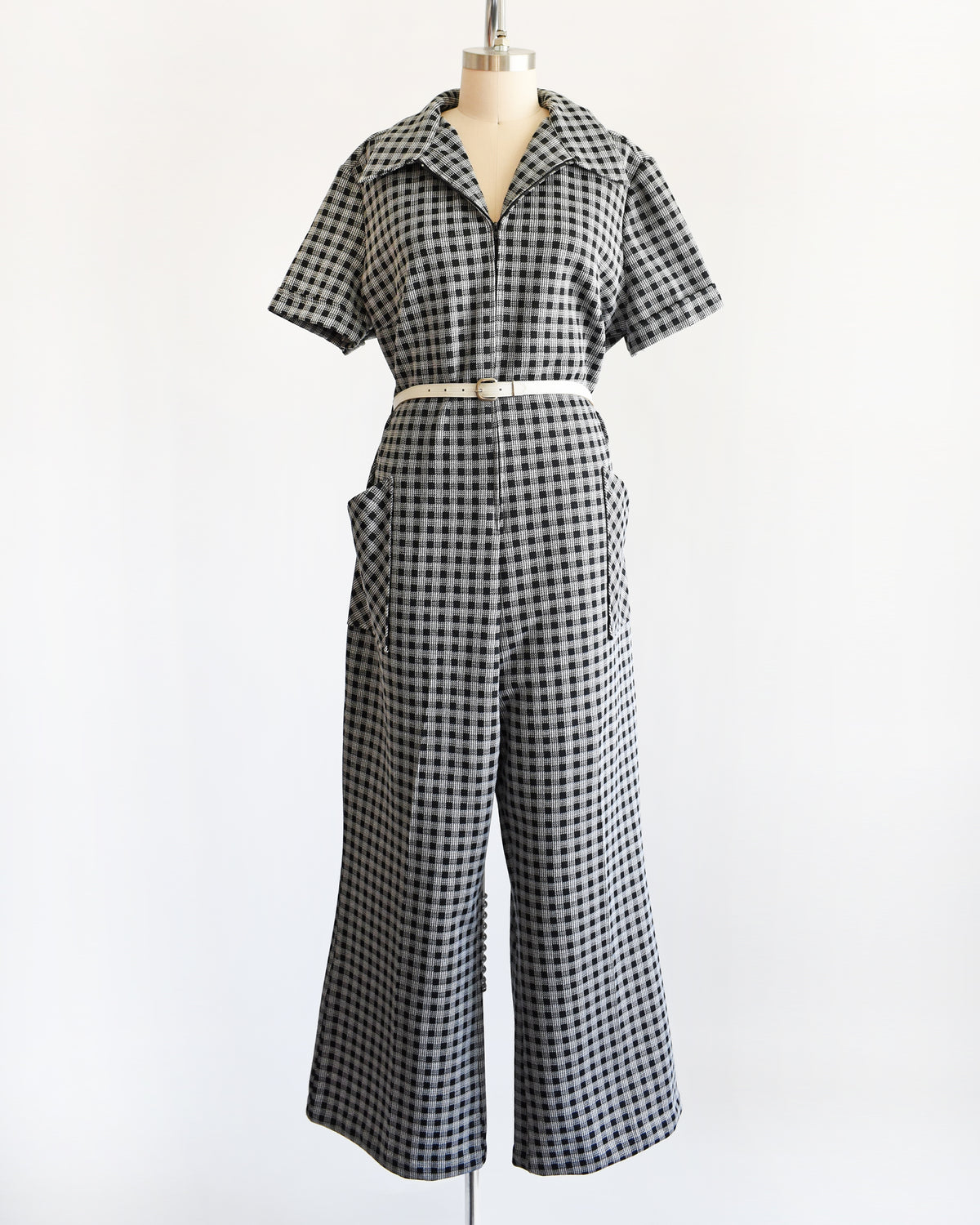 A black and white gingham short-sleeve jumpsuit displayed on a dress form mannequin against a plain white background.