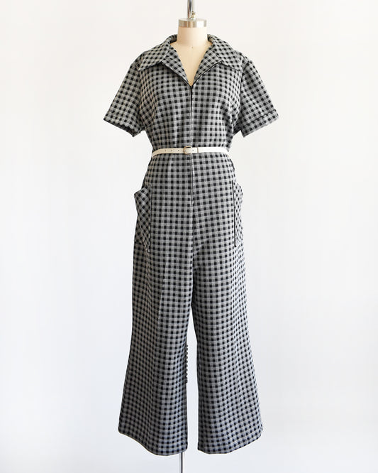 A black and white gingham short-sleeve jumpsuit displayed on a dress form mannequin against a plain white background.