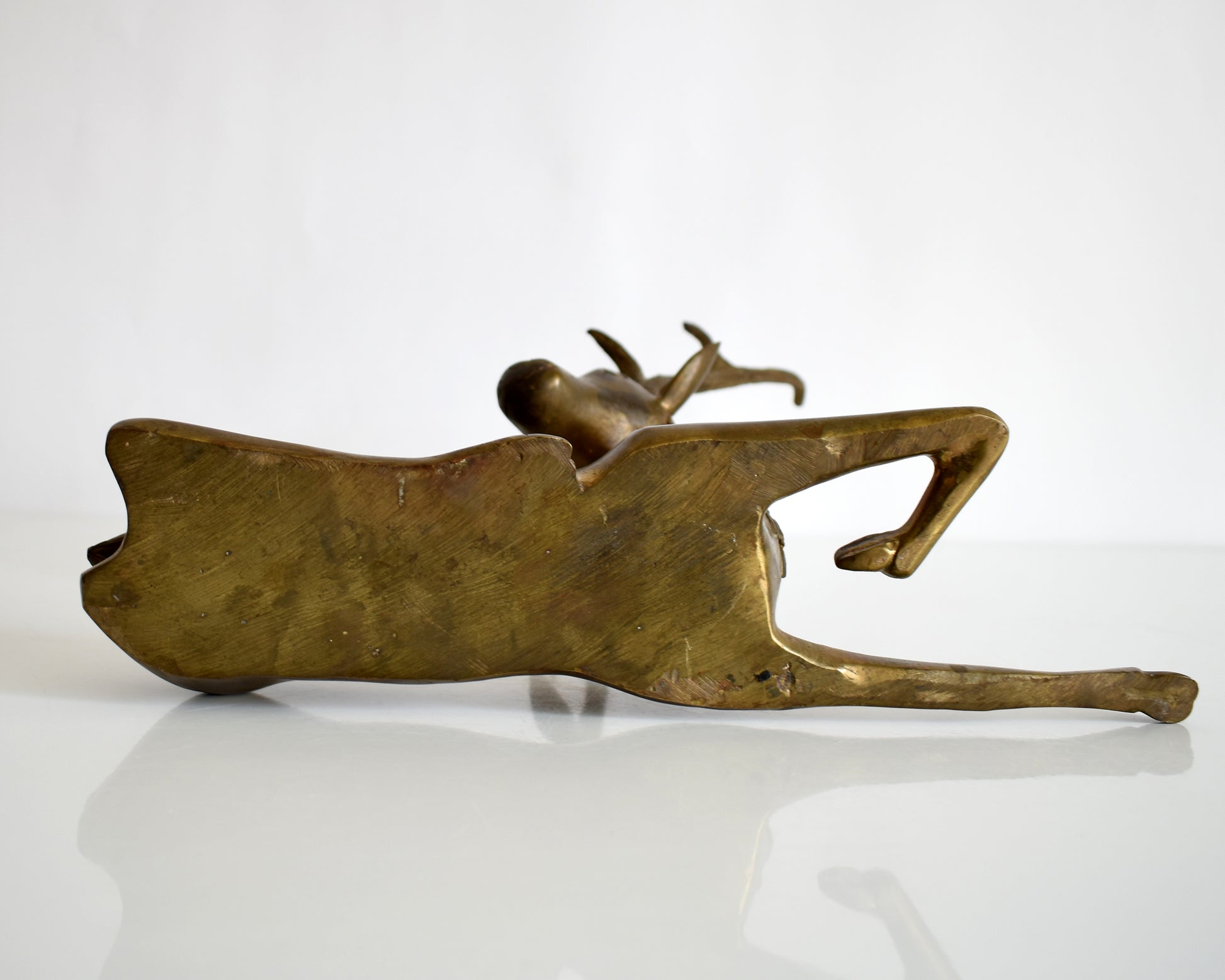 underside view of a vintage brass deer figurine on a white background