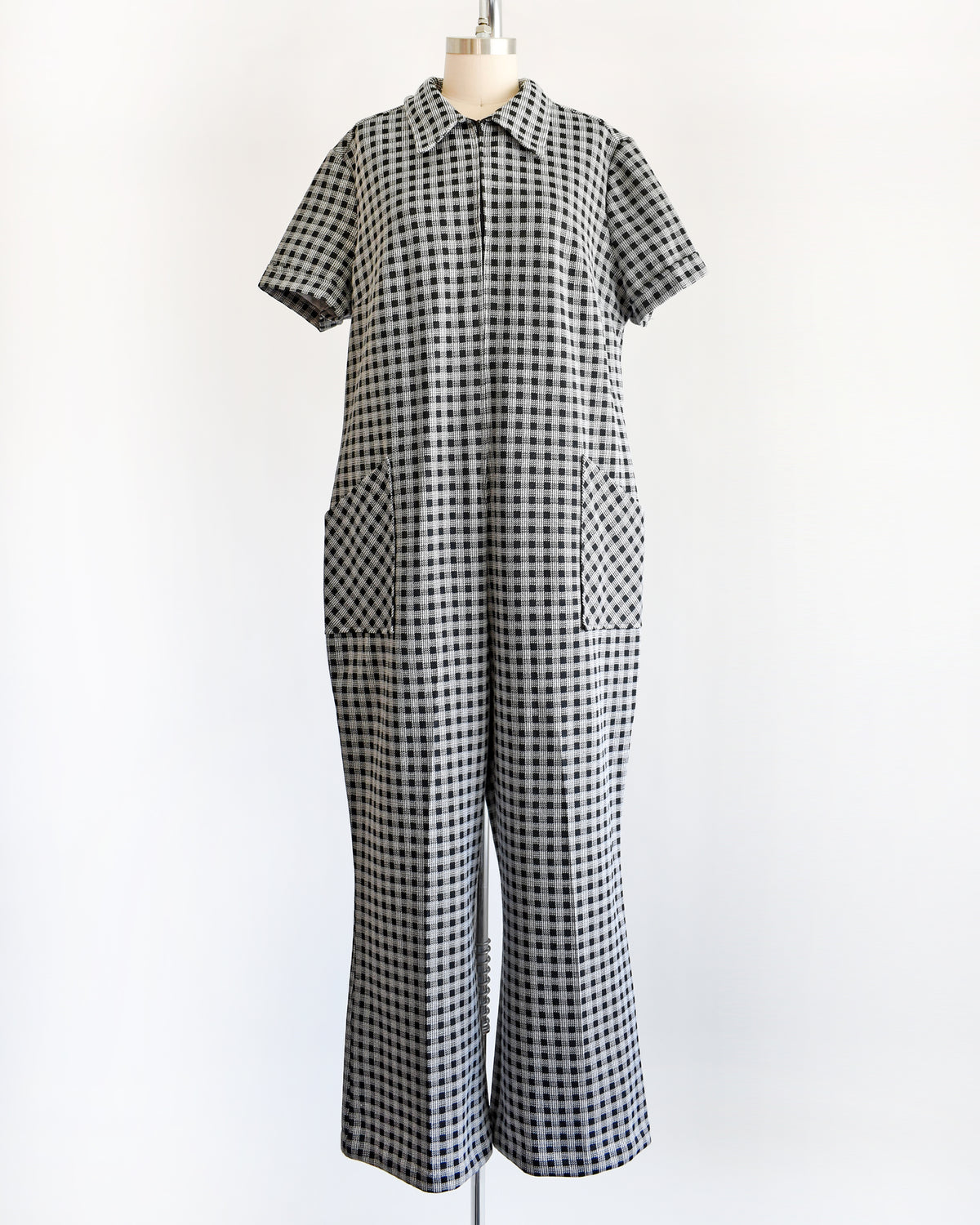 A black and white gingham short-sleeve jumpsuit displayed on a dress form mannequin against a plain white background.