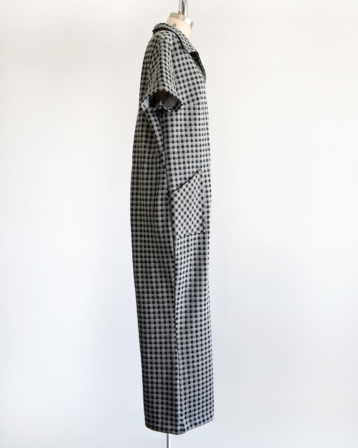 side view of a black and white gingham short-sleeve jumpsuit displayed on a dress form mannequin against a plain white background.