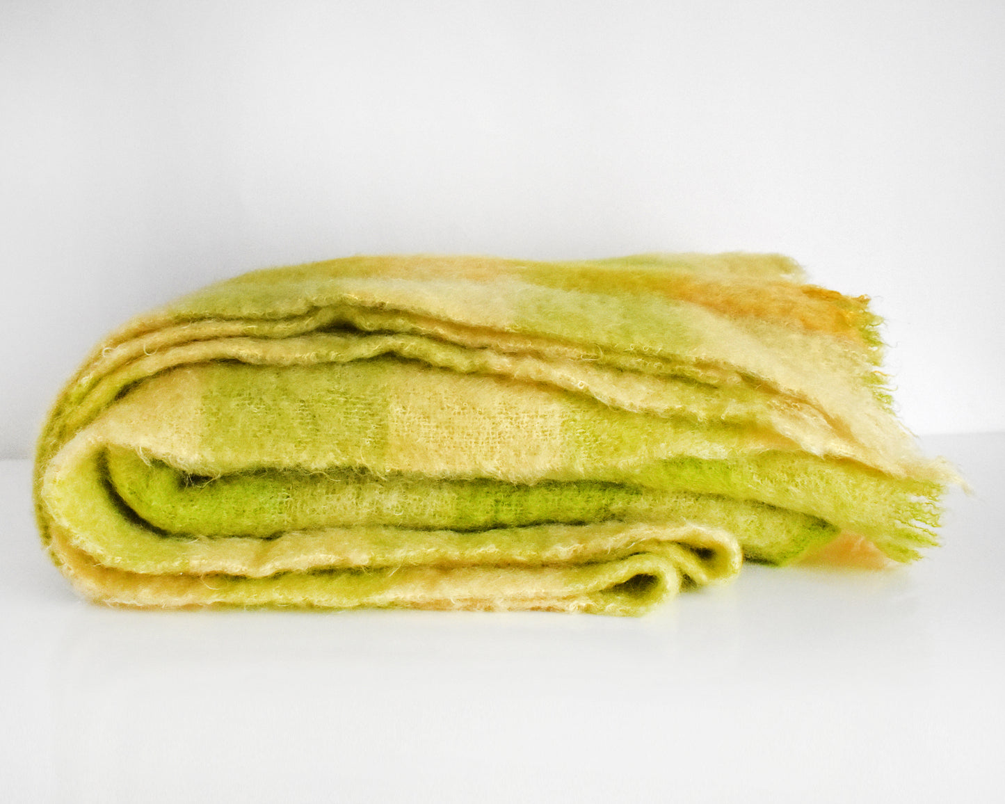 a vintage yellow and green plaid mohair wool blanket folded on a white table