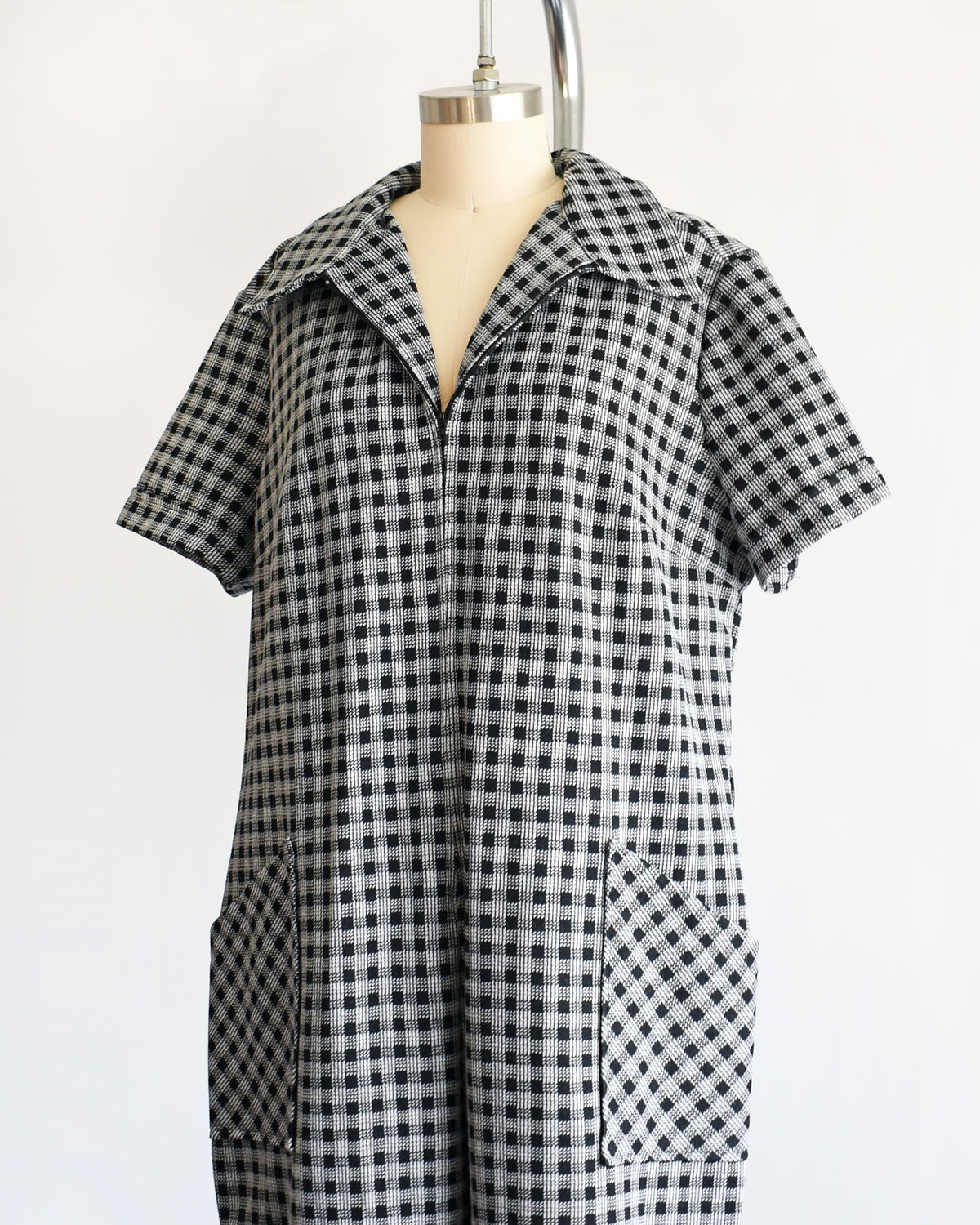 side front view of a black and white gingham short-sleeve jumpsuit displayed on a dress form mannequin against a plain white background.