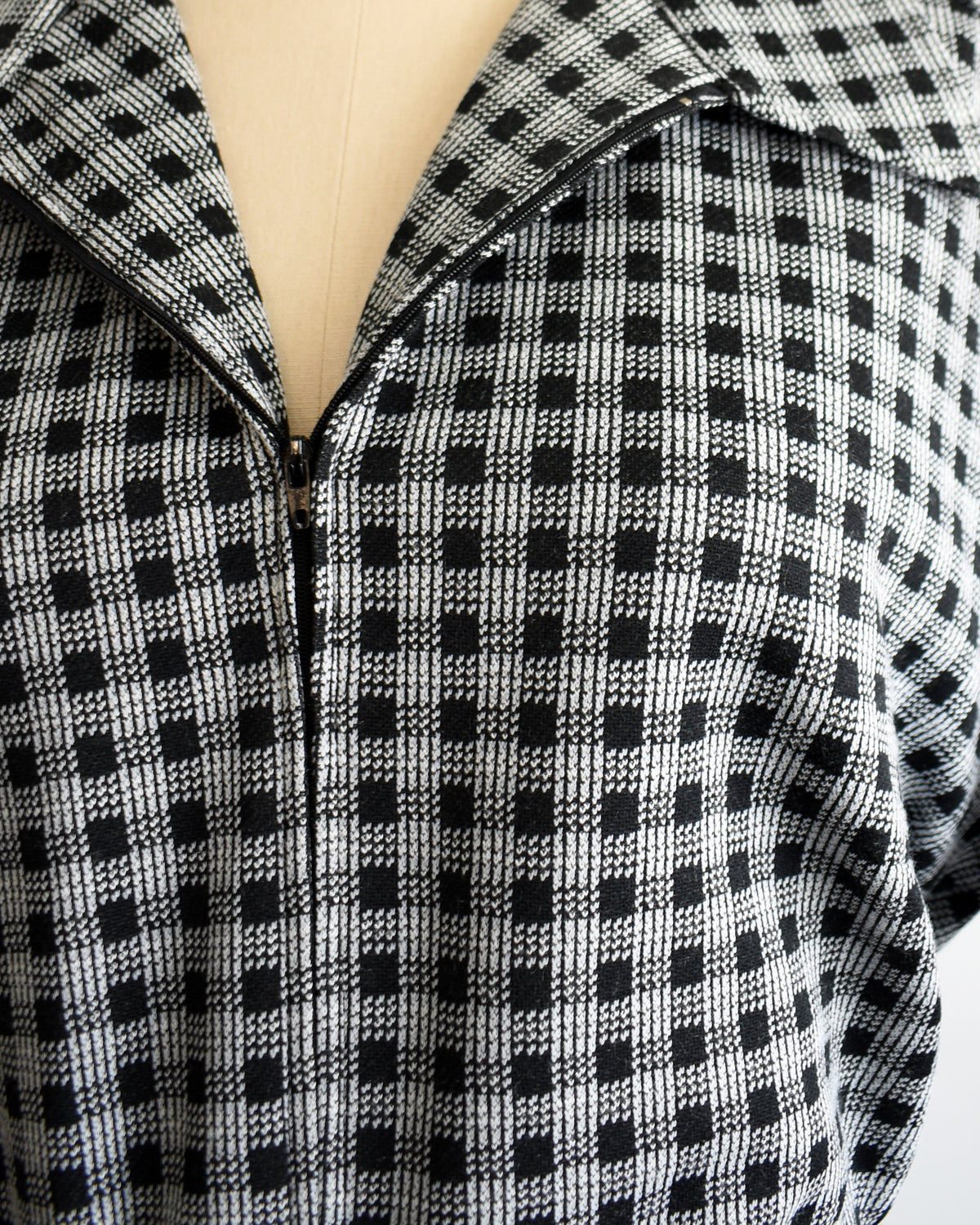 Close-up of a black and white checkered zip-up front displayed on a beige dress form mannequin.