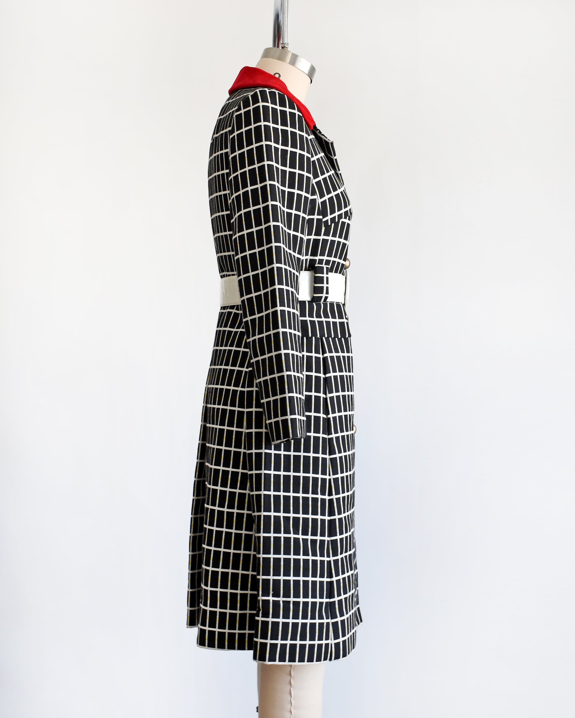 side view of a vintage 70s black and white plaid mod coat with red velvet collar and wide white belt.