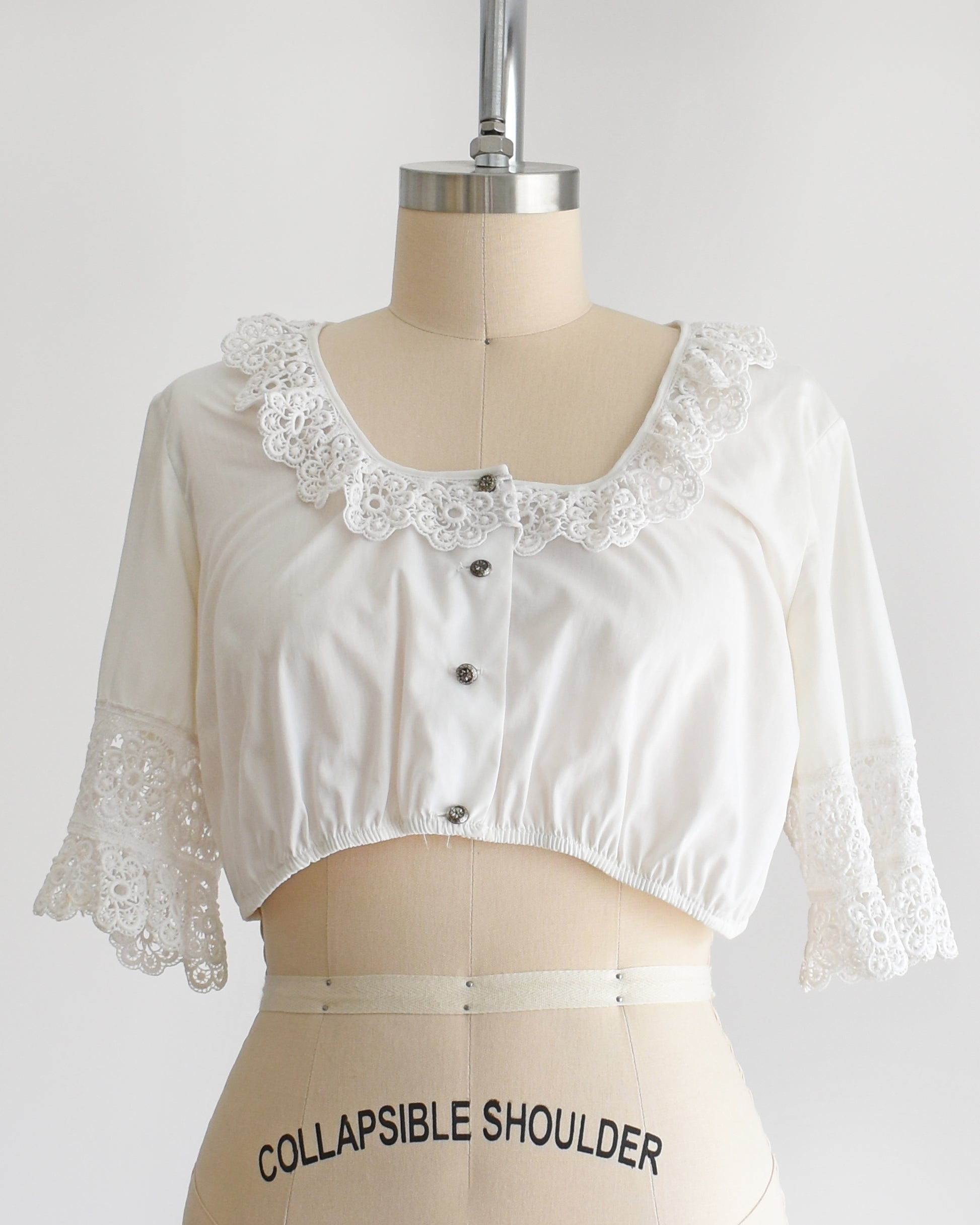 Close up of the cropped white ruffled blouse. Ruffles along the neckline and cuffs. Four silver buttons on the front.