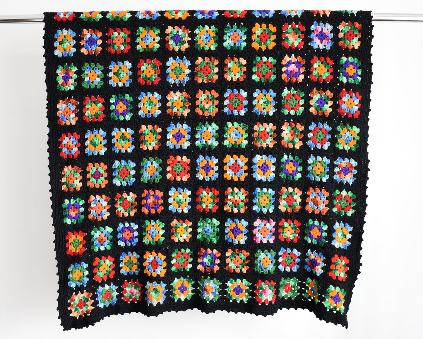 a black granny square blanket draped over a silver rod