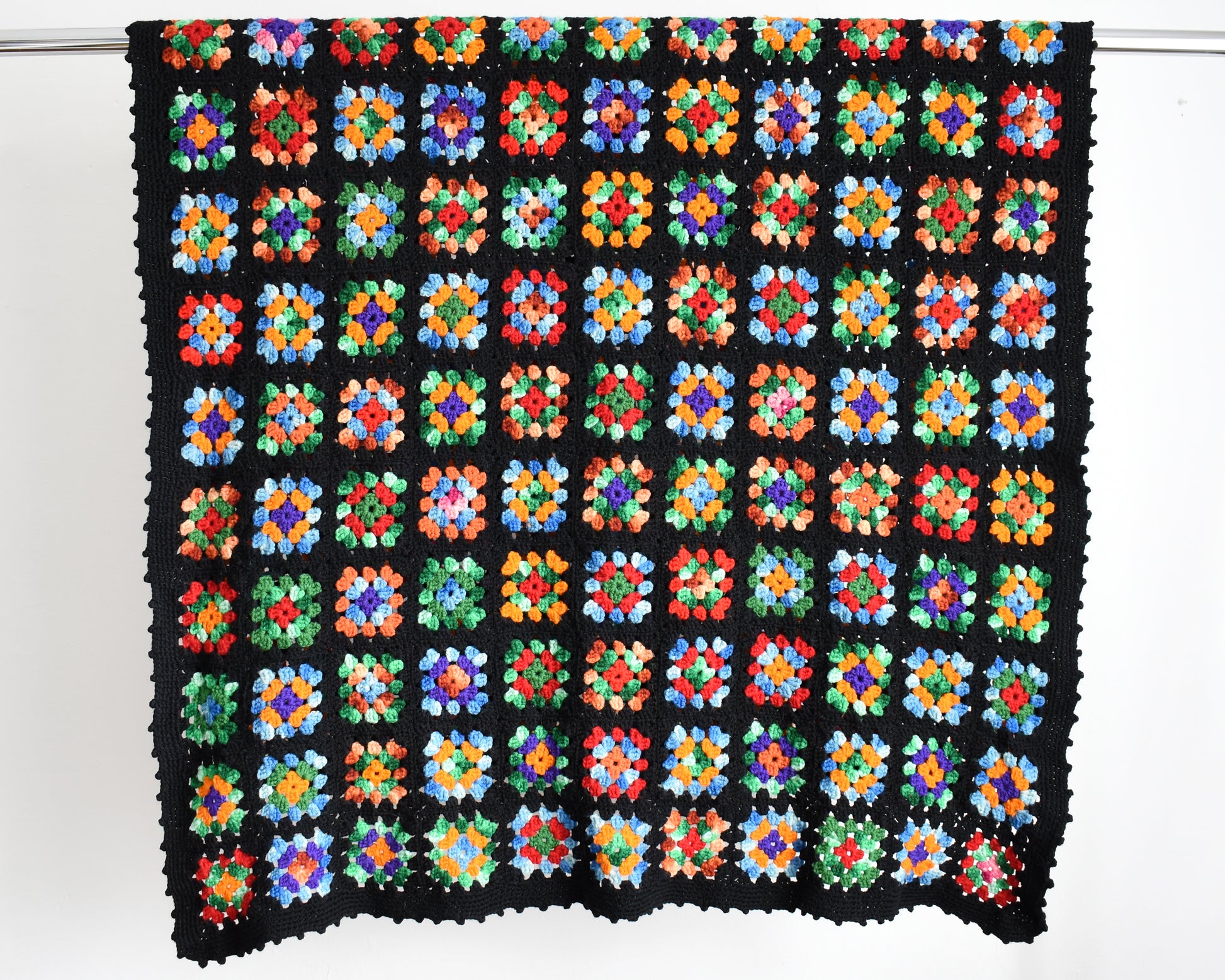 a black granny square blanket draped over a silver rod