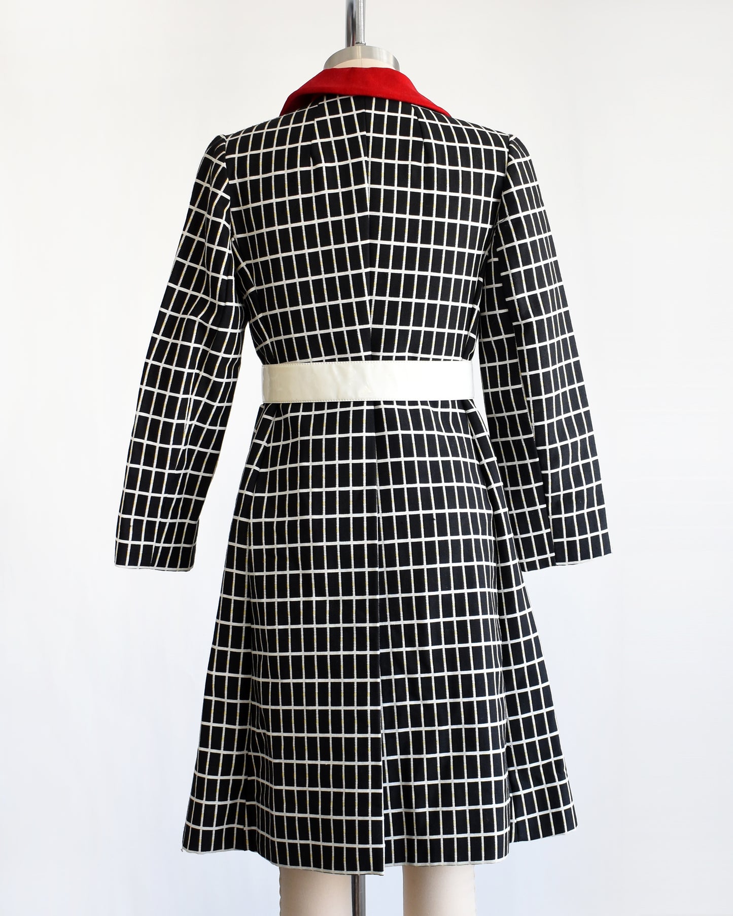 back view of a vintage 70s black and white plaid mod coat with red velvet collar and wide white belt.