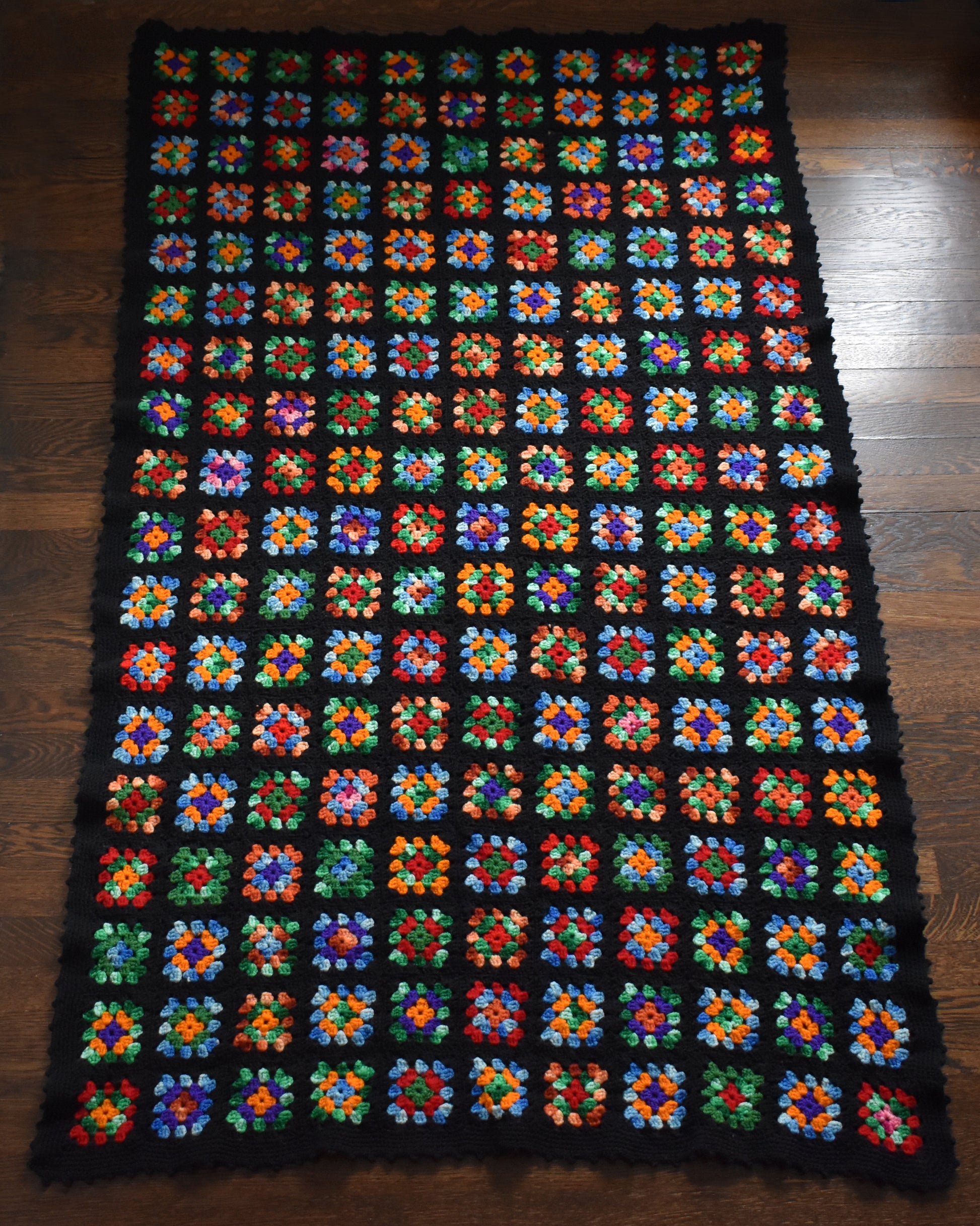 a black granny square blanket laid out on a wood floor