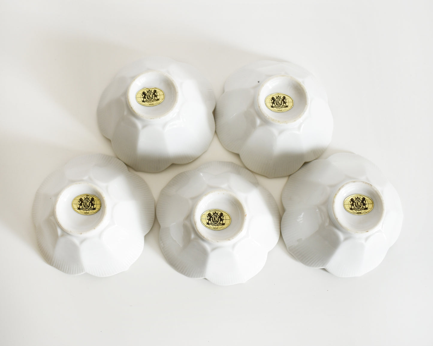 Set of five white ceramic bowls turned upside down showing their gold logos on a white background