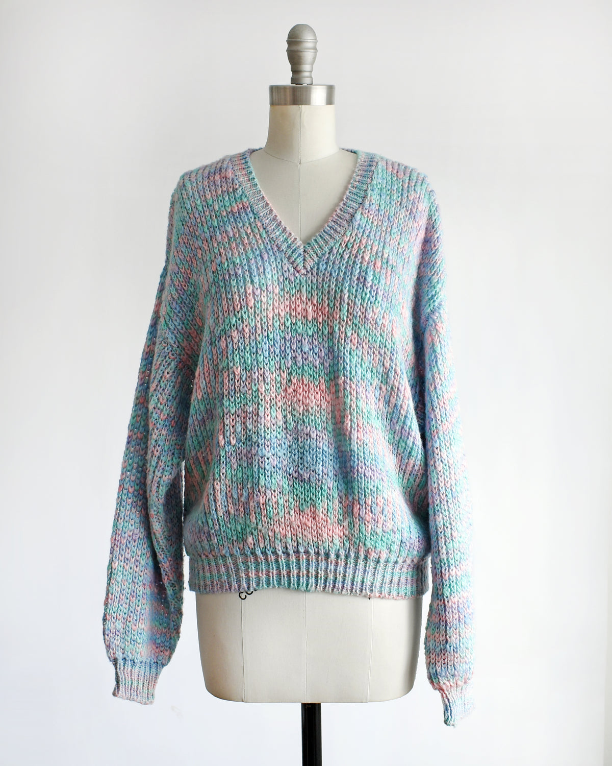 A vintage 1980s multicolor knit sweater with a V-neck and long sleeves, displayed on a cream dress form mannequin against a white background.