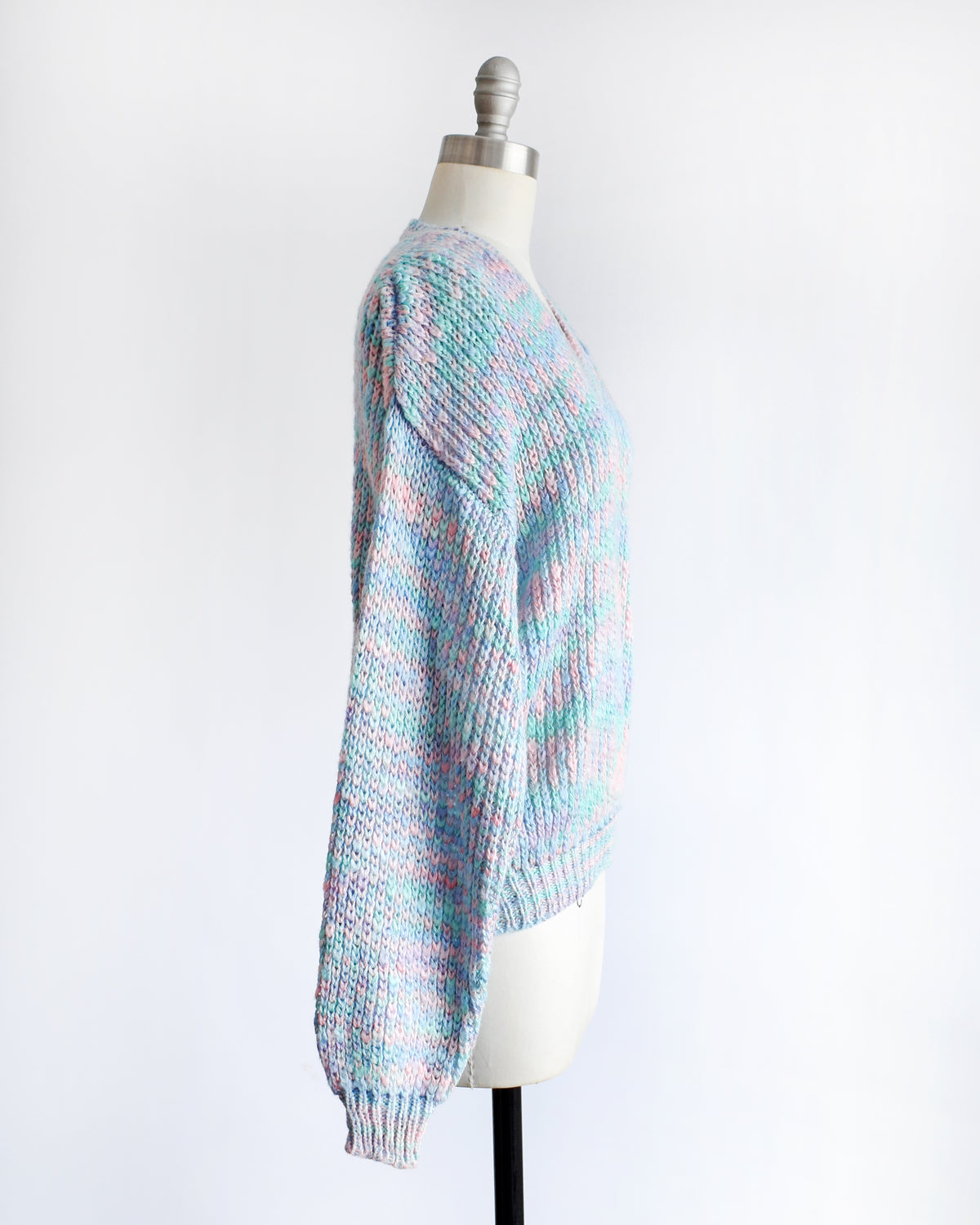 side view of a vintage 1980s multicolor knit sweater with a V-neck and long sleeves, displayed on a cream dress form mannequin against a white background.