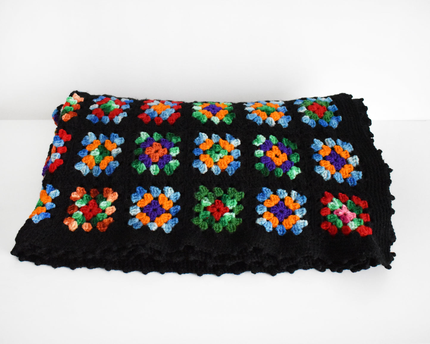 a black granny square blanket folded on a white table