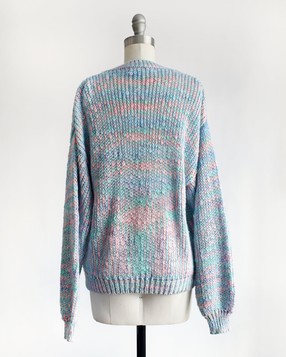 back view of a vintage 1980s multicolor knit sweater with a V-neck and long sleeves, displayed on a cream dress form mannequin against a white background.