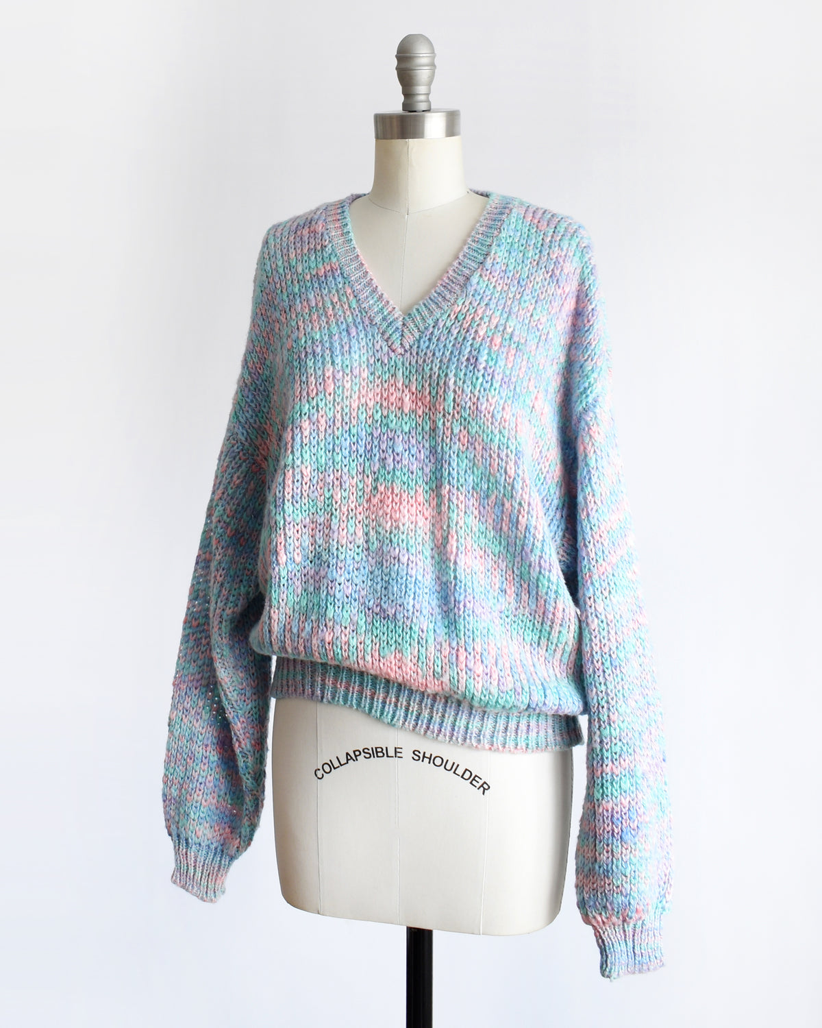 side view of a vintage 1980s multicolor knit sweater with a V-neck and long sleeves, displayed on a cream dress form mannequin against a white background.