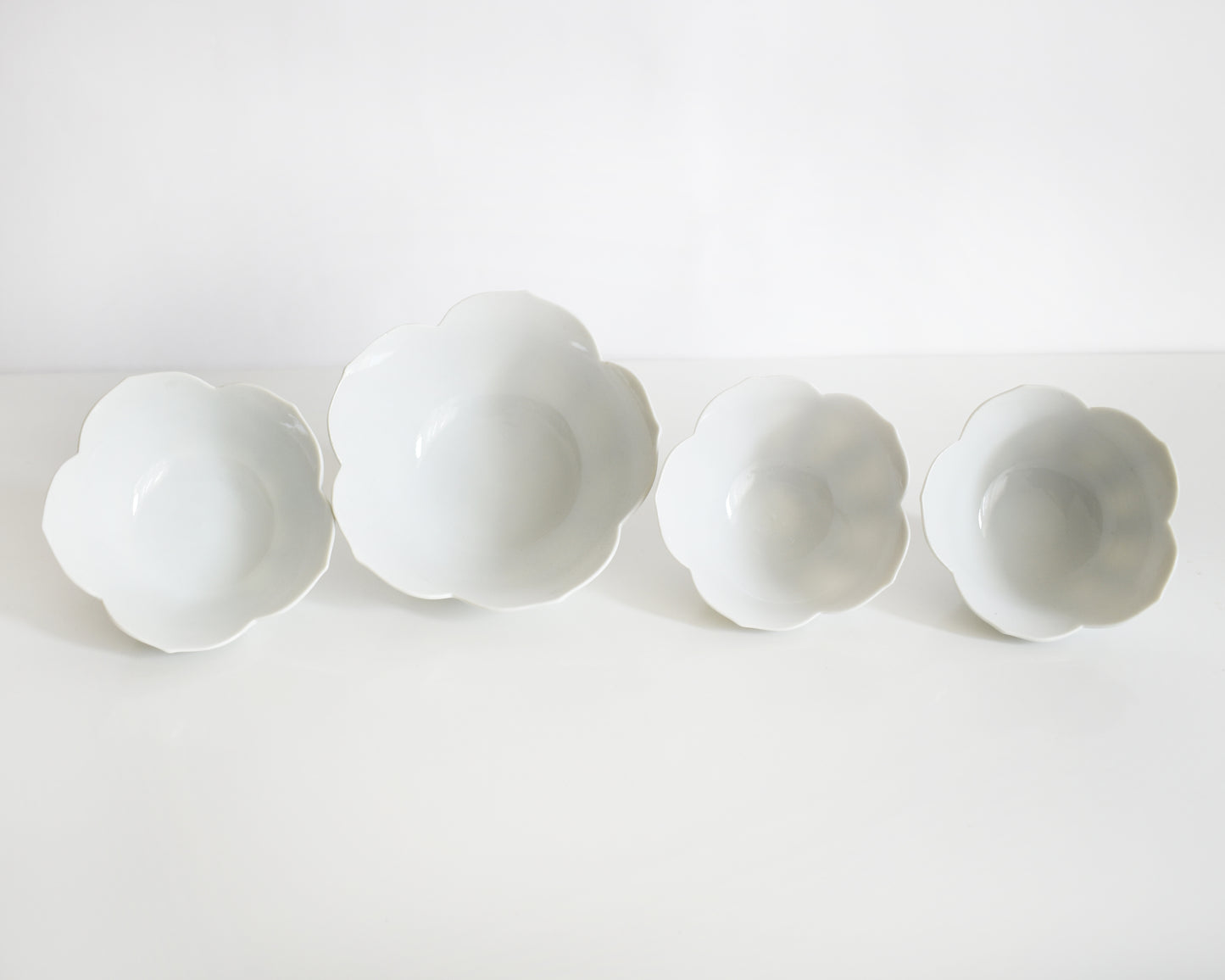 Four white ceramic flower-shaped bowls on a white background