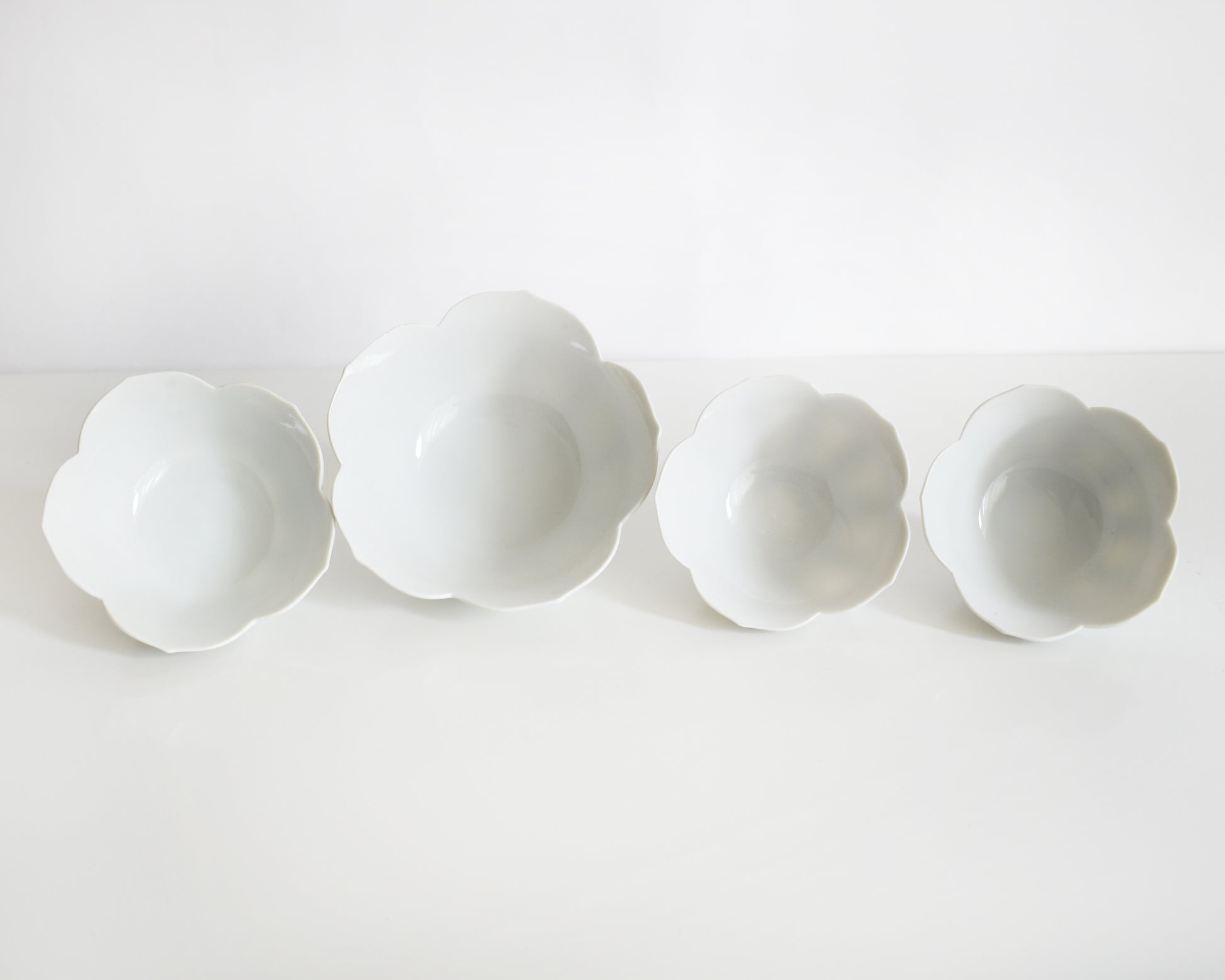 Four white ceramic flower-shaped bowls on a white background