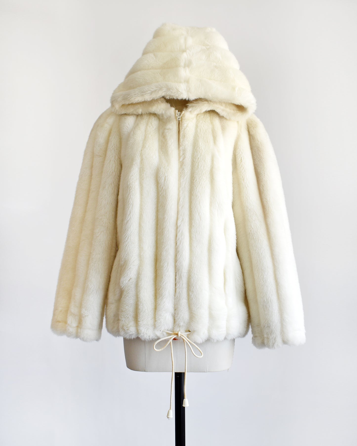 a vintage 1980s cream faux fur hooded coat with a drawstring on the bottom. the hood is pulled up on this photo/