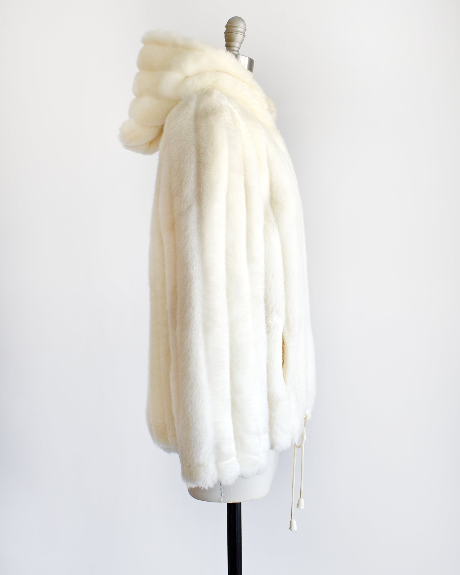 side view of a vintage 1980s cream faux fur hooded coat with a drawstring on the bottom.