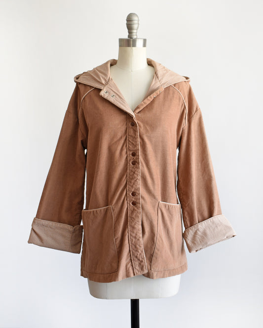 a vintage 1970s  tan corduroy hooded jacket with button-front closure and large front patch pockets, displayed on a cream dress form against a plain white background.