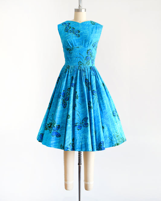 A vintage 1950s Anne Fogarty blue fit and flare dress that has a butterfly print. The dress is on a dress form.