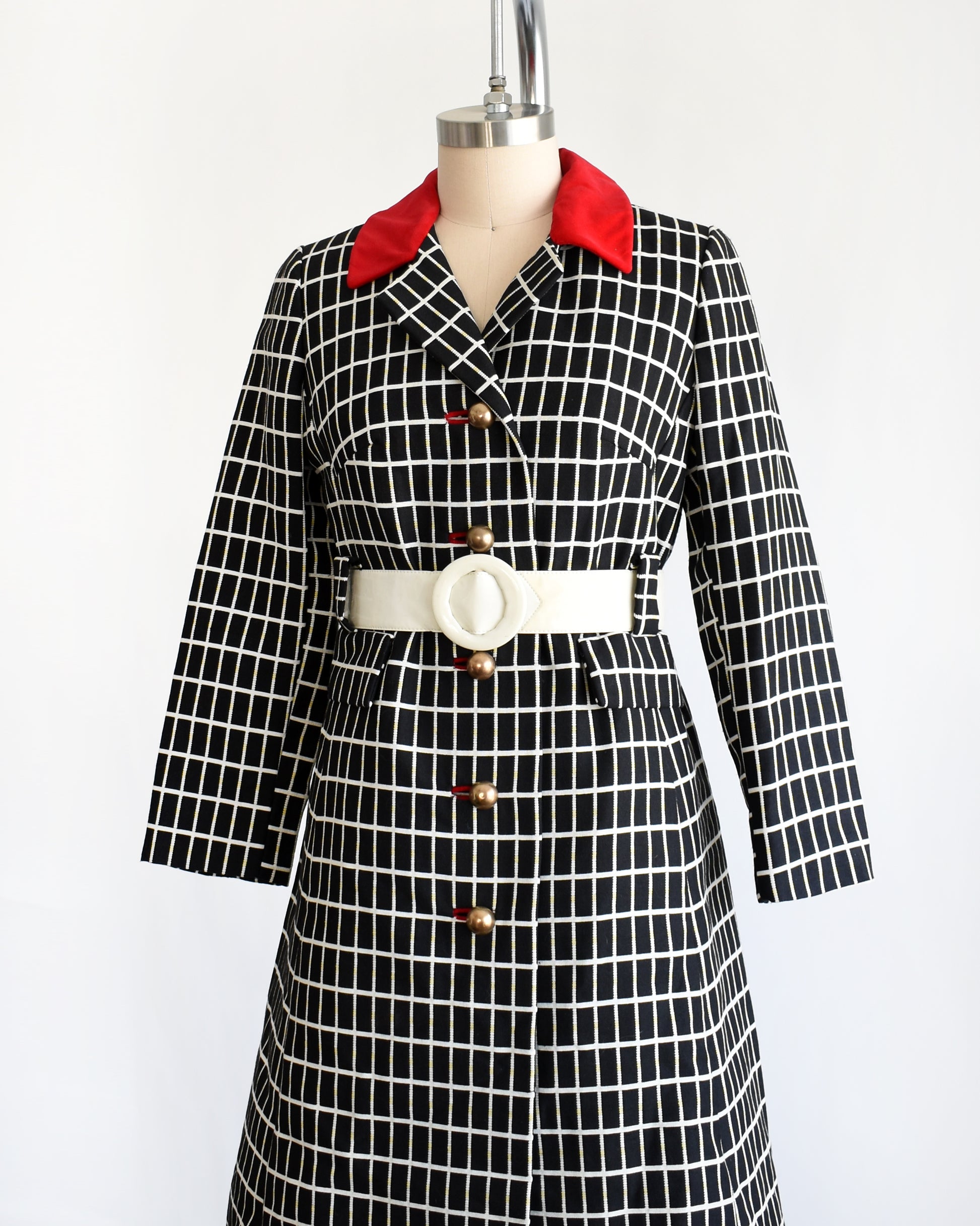 side front view of a vintage 70s black and white plaid mod coat with red velvet collar and wide white belt.