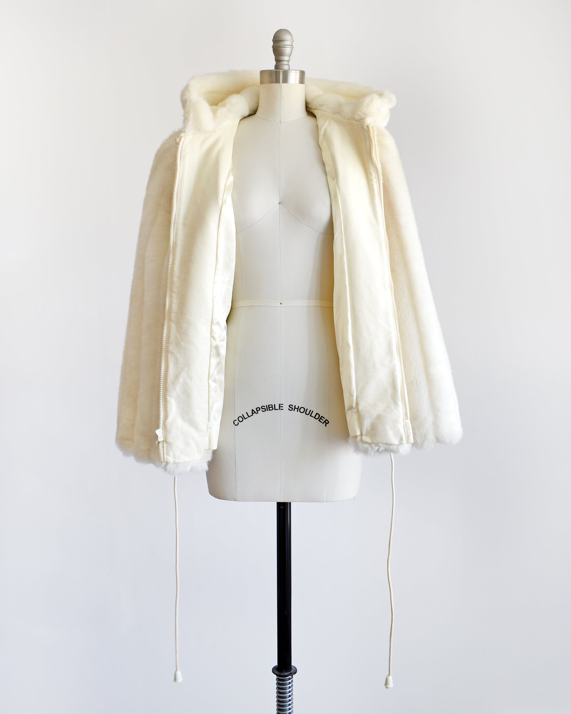 a vintage 1980s cream faux fur hooded coat with a drawstring on the bottom. the coat is zipped open showing the cream acetate lining and faux leather trim.