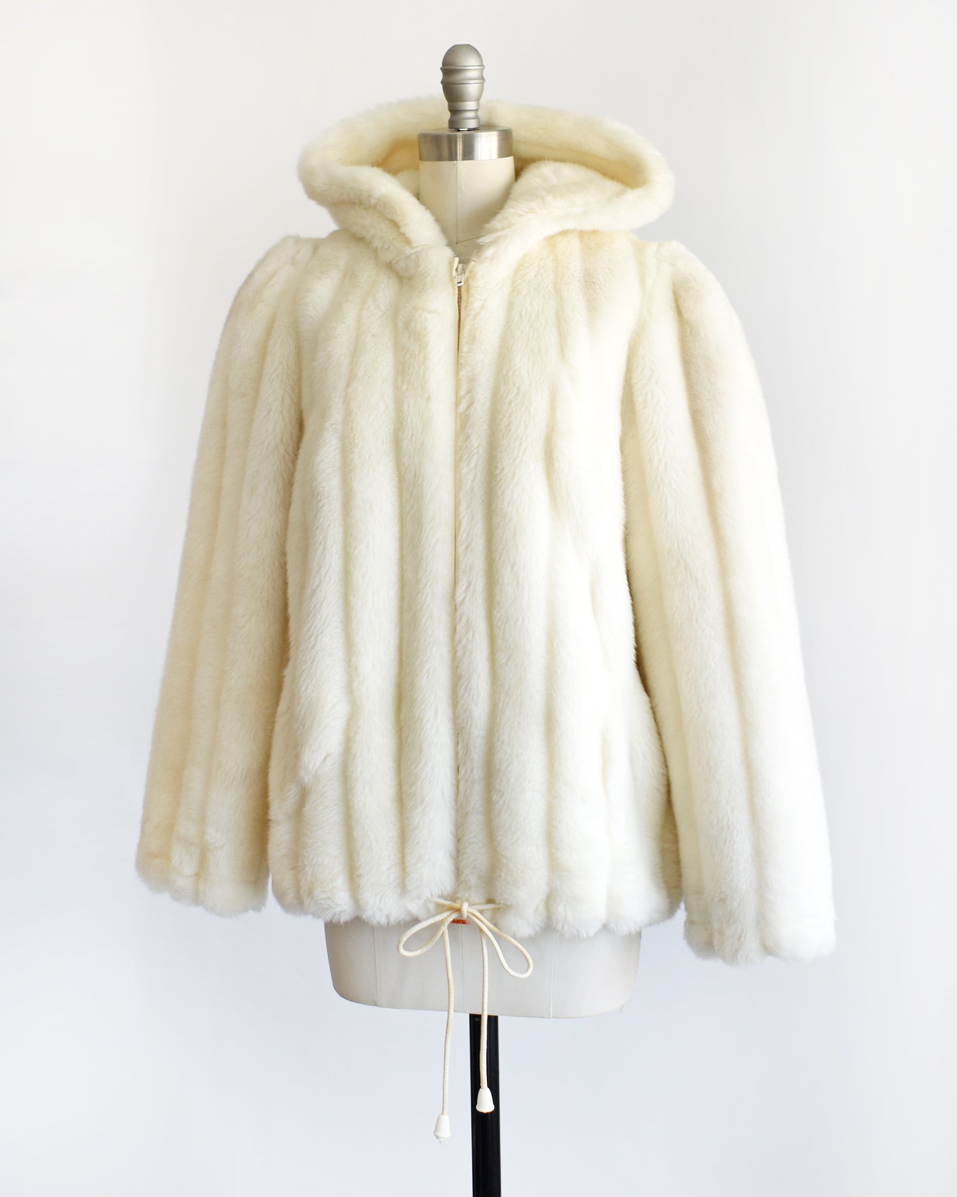 side front view of a vintage 1980s cream faux fur hooded coat with a drawstring on the bottom.