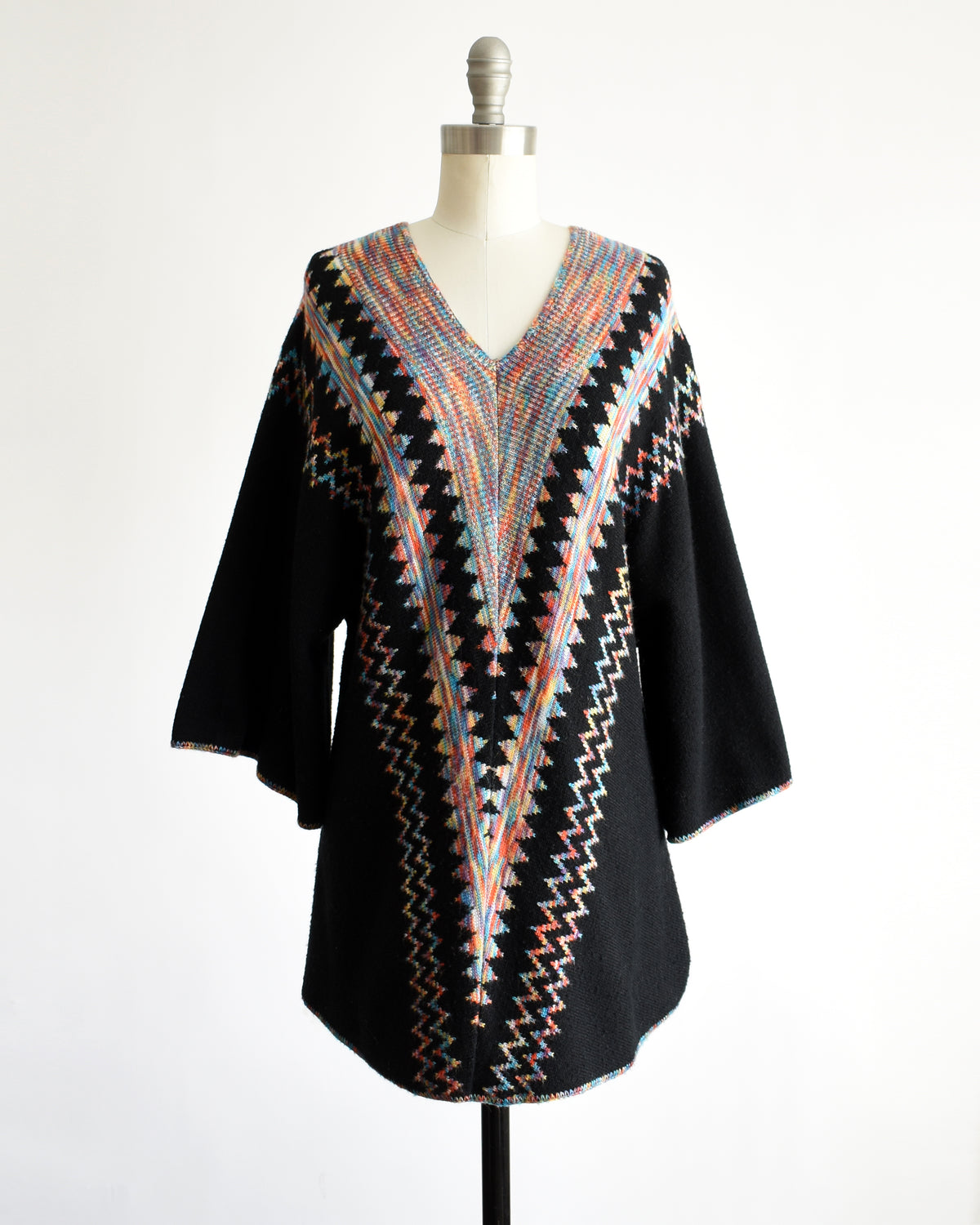 a vintage 1970s  black three-quarter sleeve tunic top with a colorful geometric zigzag pattern down the front, displayed on a mannequin against a white background.