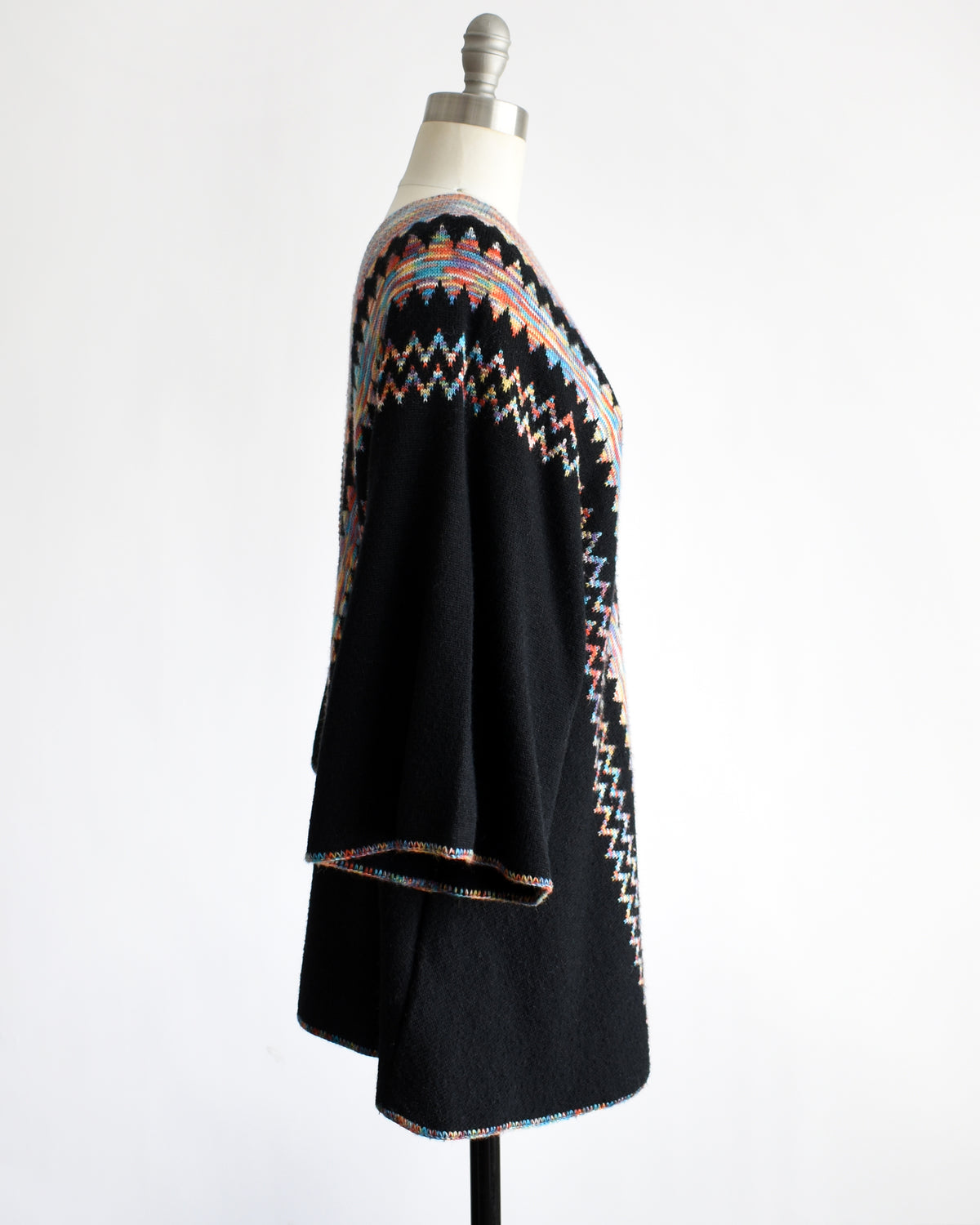 side view of a vintage 1970s  black three-quarter sleeve tunic top with a colorful geometric zigzag pattern down the front, displayed on a mannequin against a white background.