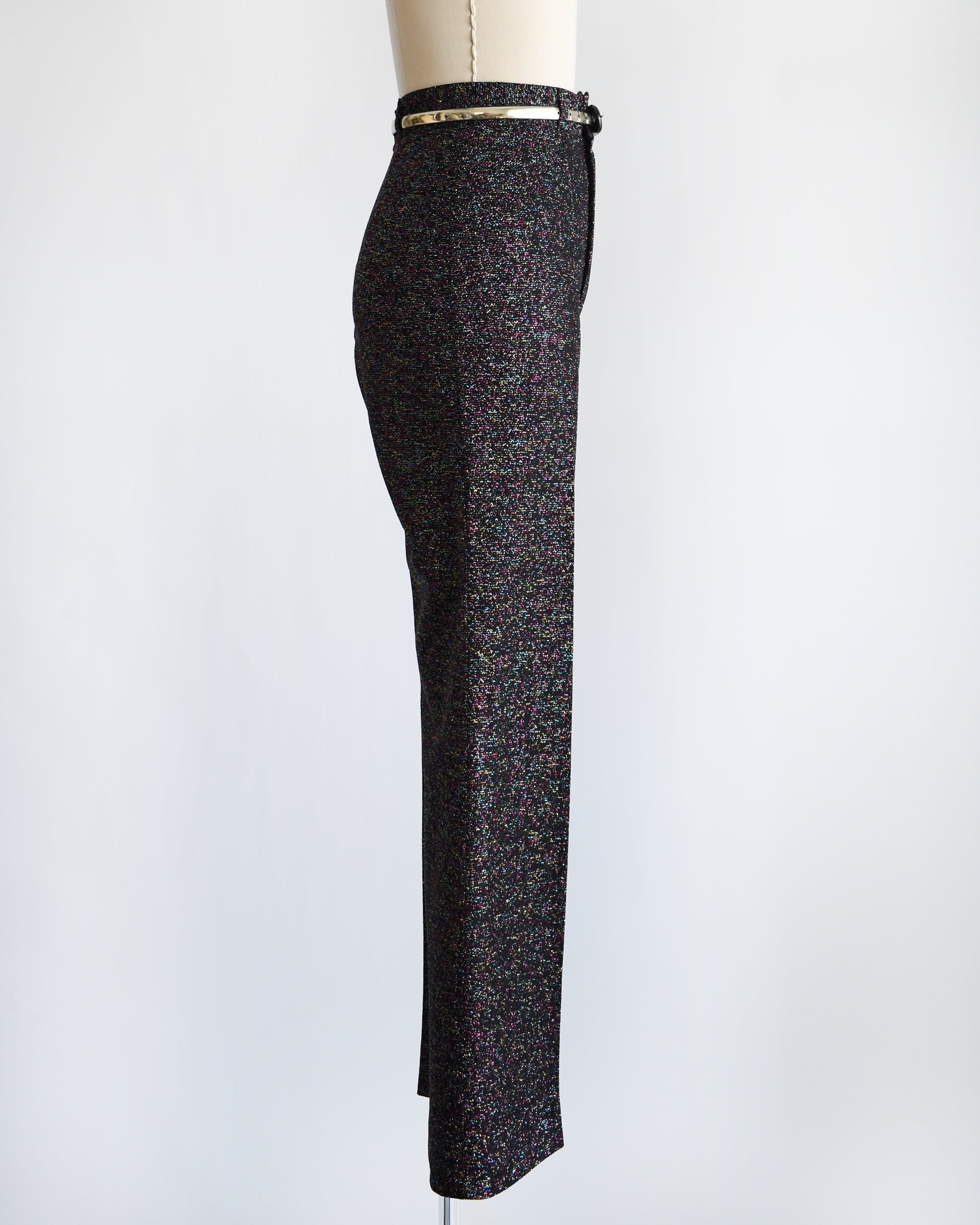side view of a pair of vintage 1970s black rainbow metallic pants with a silver belt on a mannequin against a white background